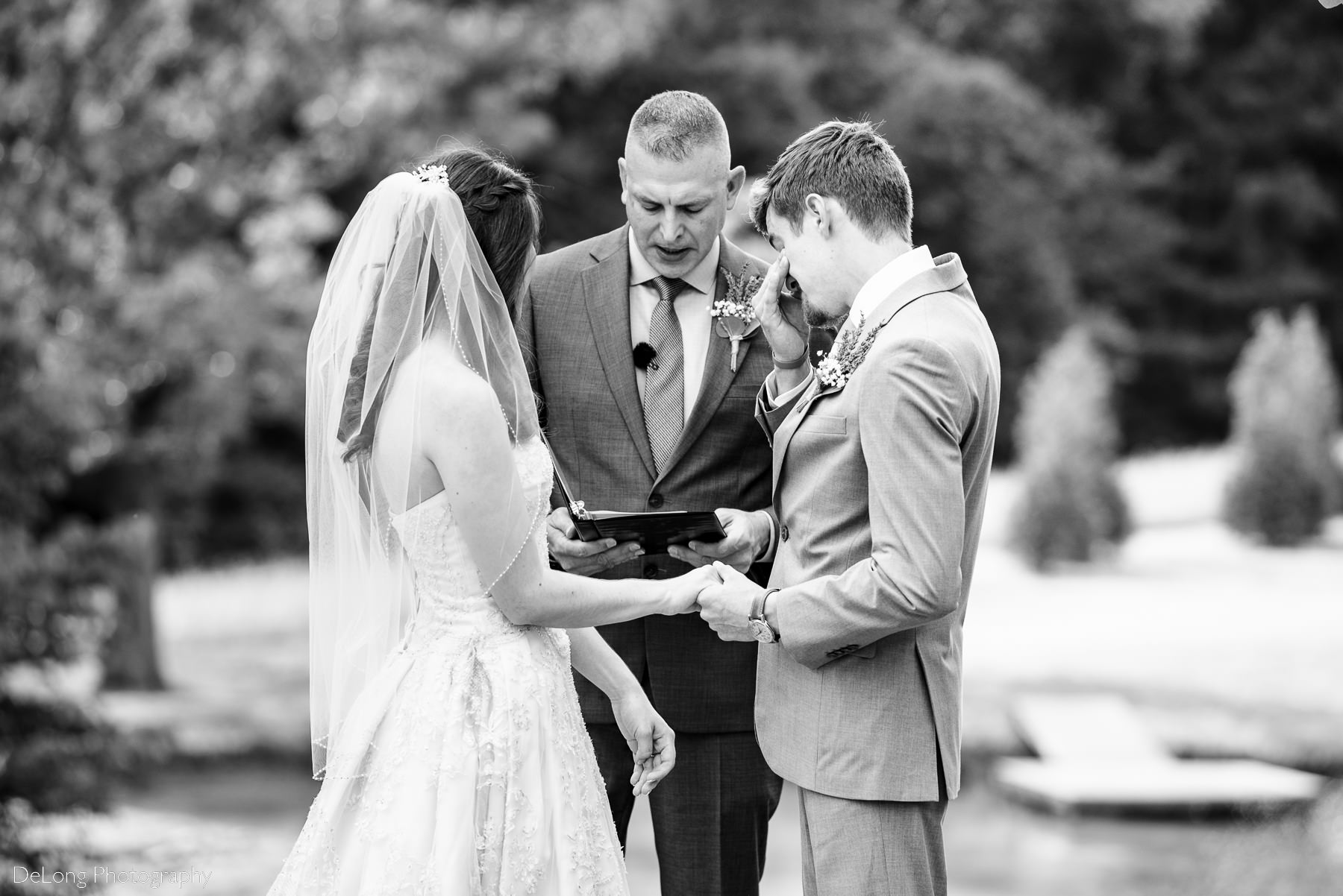 Black and white image of groom wiping tears during wedding ceremony at Lady Bird Farms by Charlotte Wedding Photographers DeLong Photography