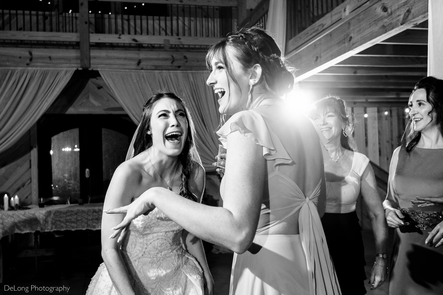 Black and white image of bride and her sister cracking up laughing on the dance floor of the wedding reception at Lady Bird Farms by Charlotte Wedding Photographers DeLong Photography