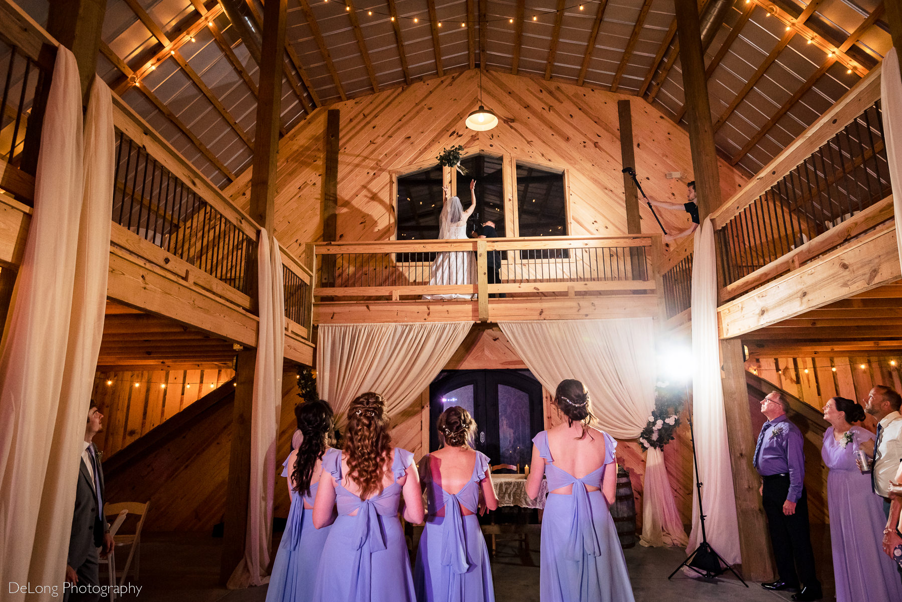 Bride tossing bouquet off of upper floor down to her bridesmaids at Lady Bird Farms by Charlotte Wedding Photographers DeLong Photography