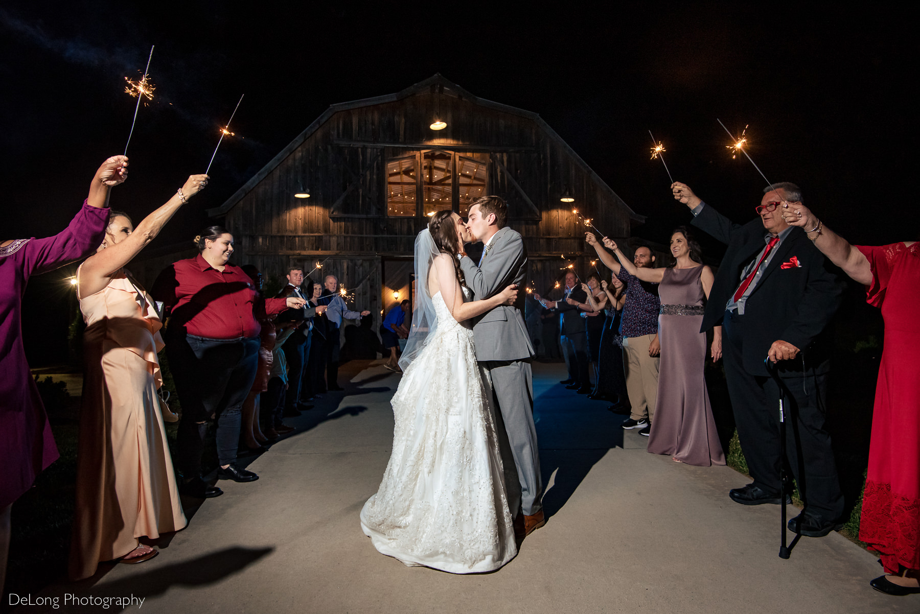 Bride and groom sharing a kiss during their sparkler exit at Lady Bird Farms by Charlotte Wedding Photographers DeLong Photography