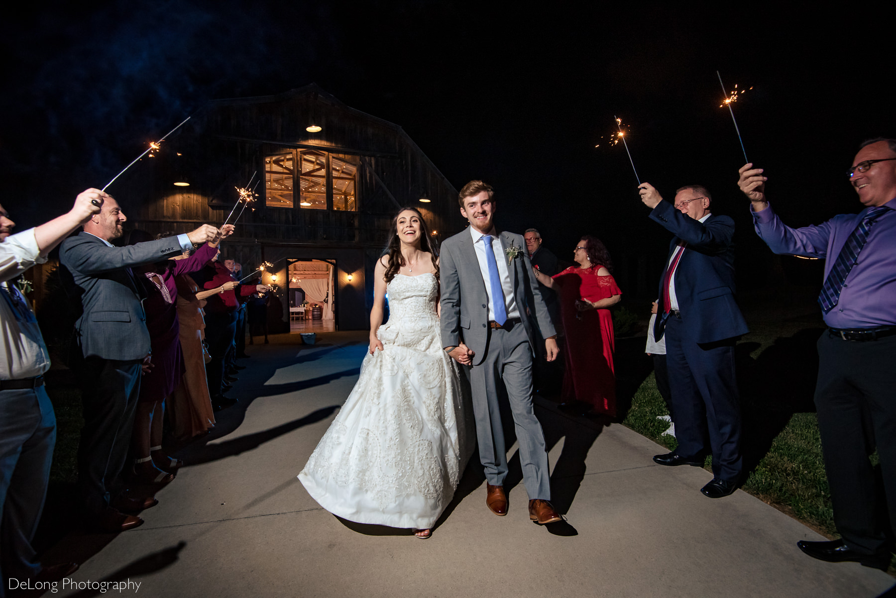 Bride and groom smiling walking out during their sparkler exit at Lady Bird Farms by Charlotte Wedding Photographers DeLong Photography