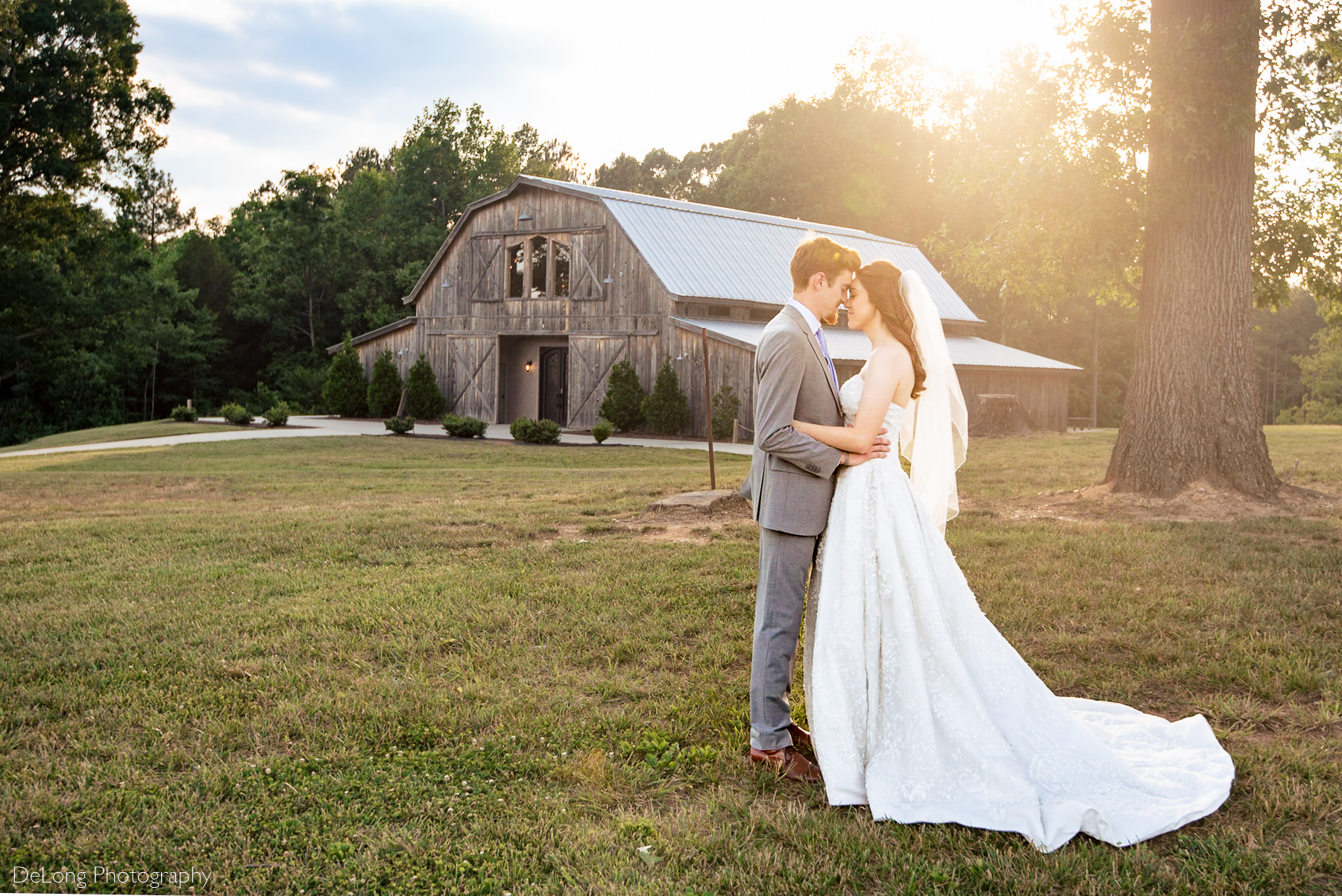 Outdoor portrait of bride and groom snuggling close with their foreheads together during sunset showing the barn in the background at Lady Bird Farms by Charlotte Wedding Photographers DeLong Photography