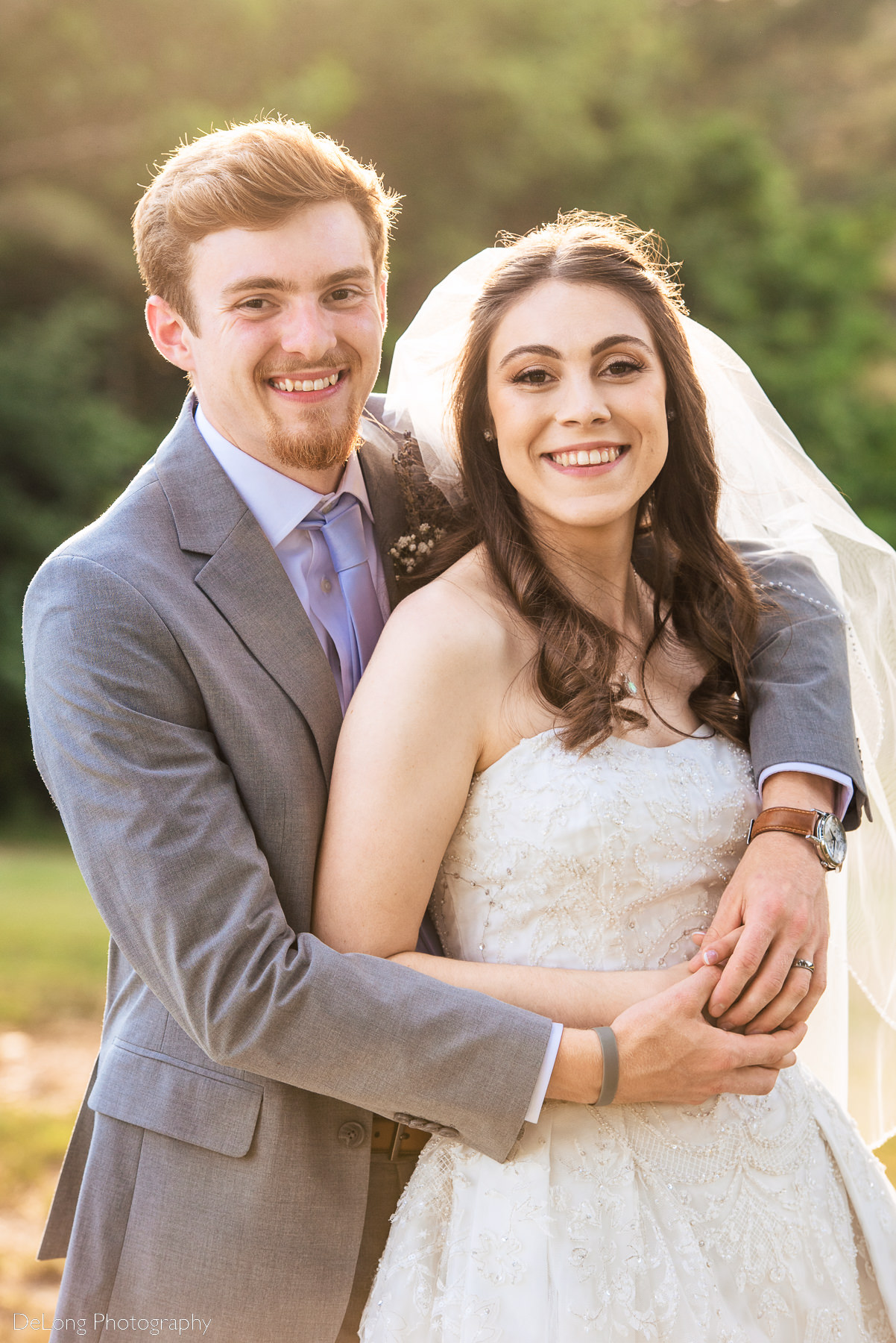 Traditional look-at-the-camera portrait of bride and groom, his arms wrapped around her during golden hour at Lady Bird Farms by Charlotte Wedding Photographers DeLong Photography