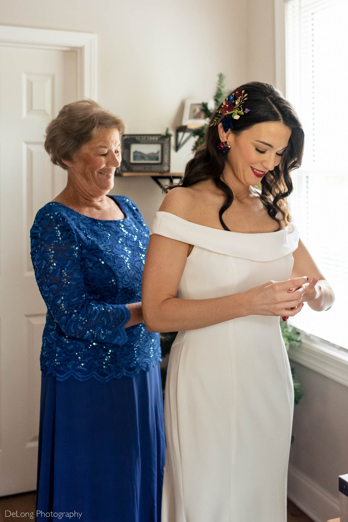 Bride adjusting her engagement ring as her mother buttons up her wedding dress by Charlotte wedding photographers DeLong Photography