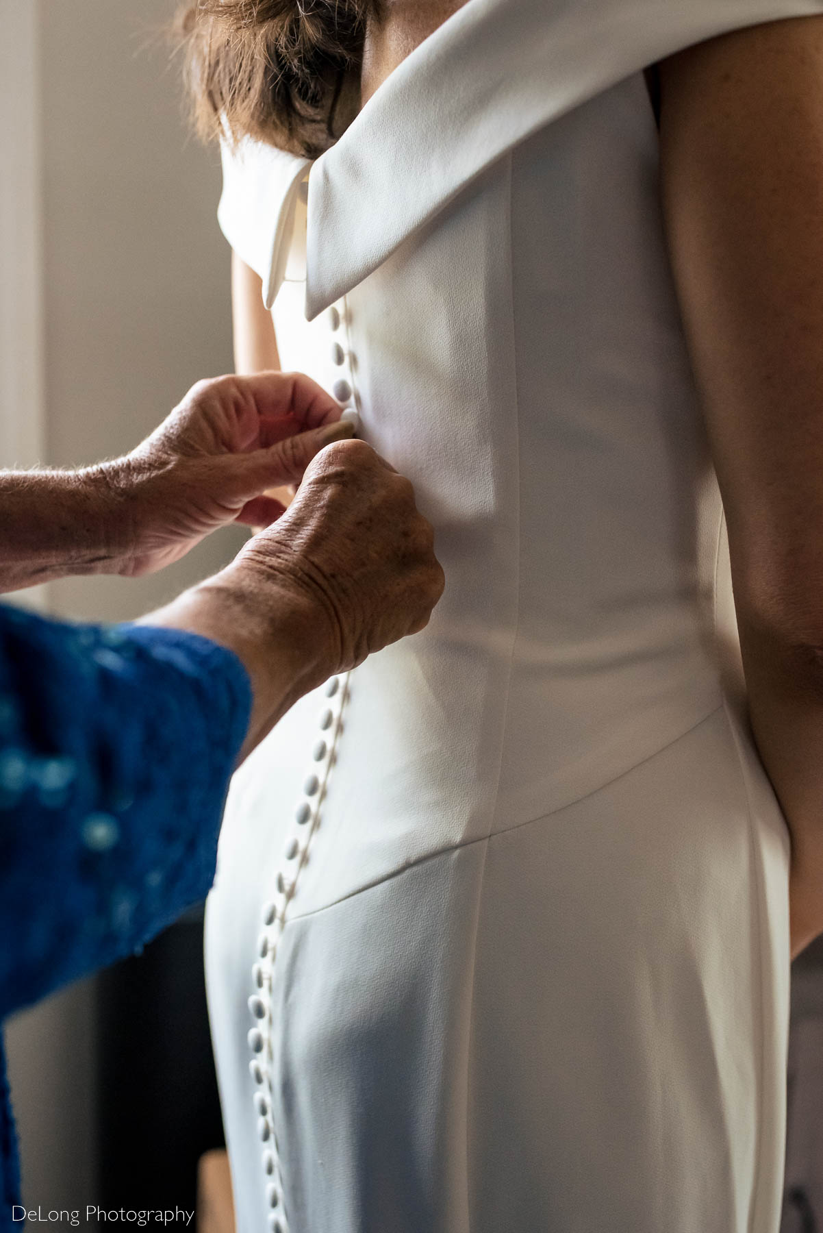 A close up of a mother of the bride's hands as she buttons up the bride's dress by Charlotte wedding photographers DeLong Photography