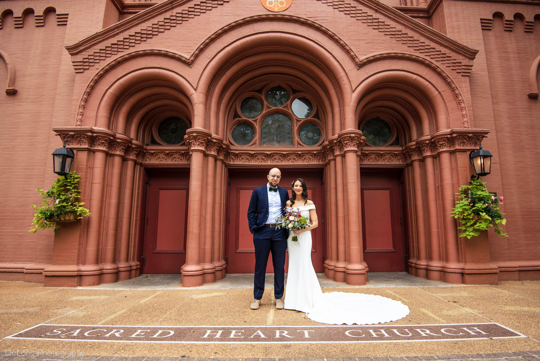 A portrait of a bride and groom in front of the "Sacred Heart Church" lettering on the ground outside the Basilica of the Sacred Heart of Jesus in Atlanta, GA by Charlotte wedding photographers DeLong Photography