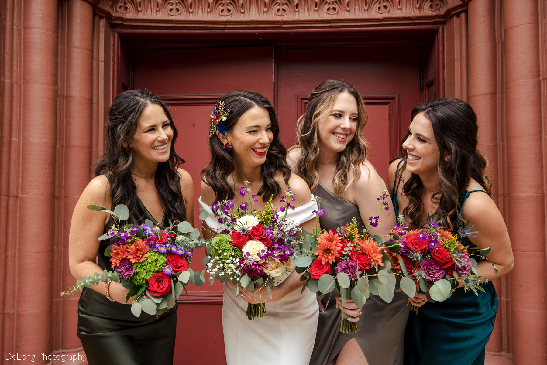 Bride smiling and laughing together with her bridesmaids with colorful jewel-toned bouquets outside the Basilica of the Sacred Heart of Jesus in Atlanta, GA by Charlotte wedding photographers DeLong Photography 