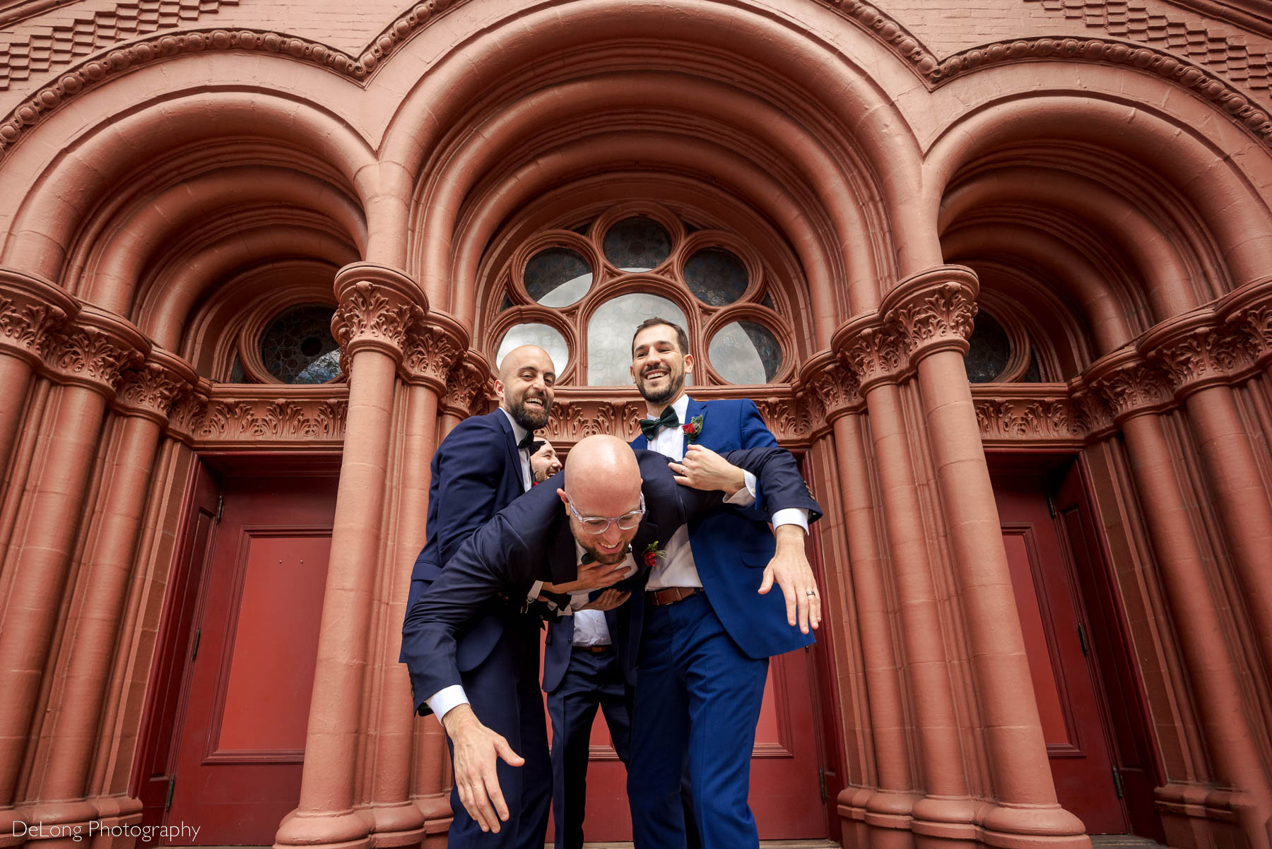 Groomsmen having fun picking up groom outside the arched doorway of the Basilica of the Sacred Heart of Jesus in Atlanta, GA by Charlotte wedding photographers DeLong Photography 