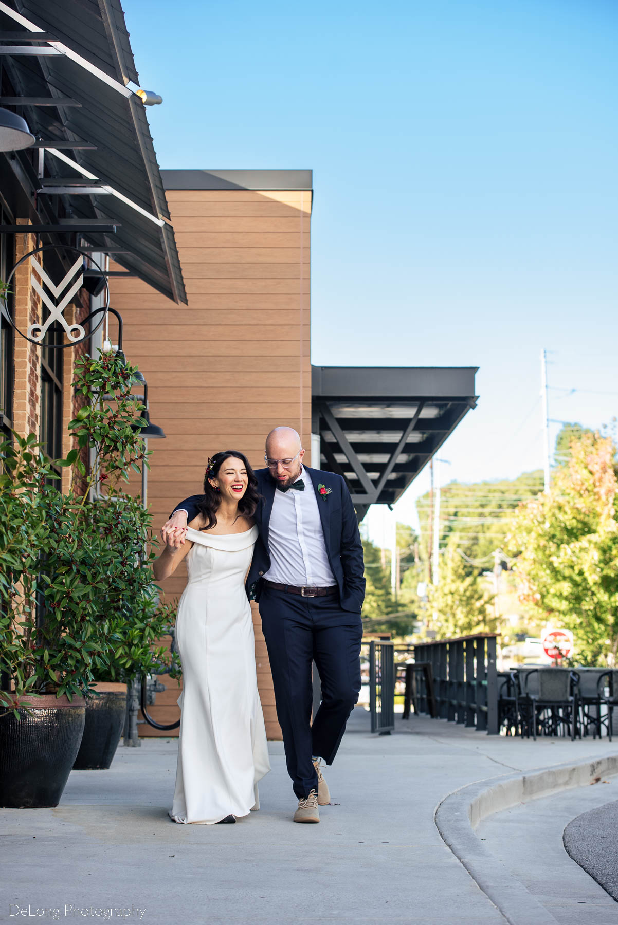 Bride and groom walking down a sidewalk, the groom's arm over the brides shoulder, bride is is laughing outside Eventide Brewing in Atlanta, GA by Charlotte wedding photographers DeLong Photography