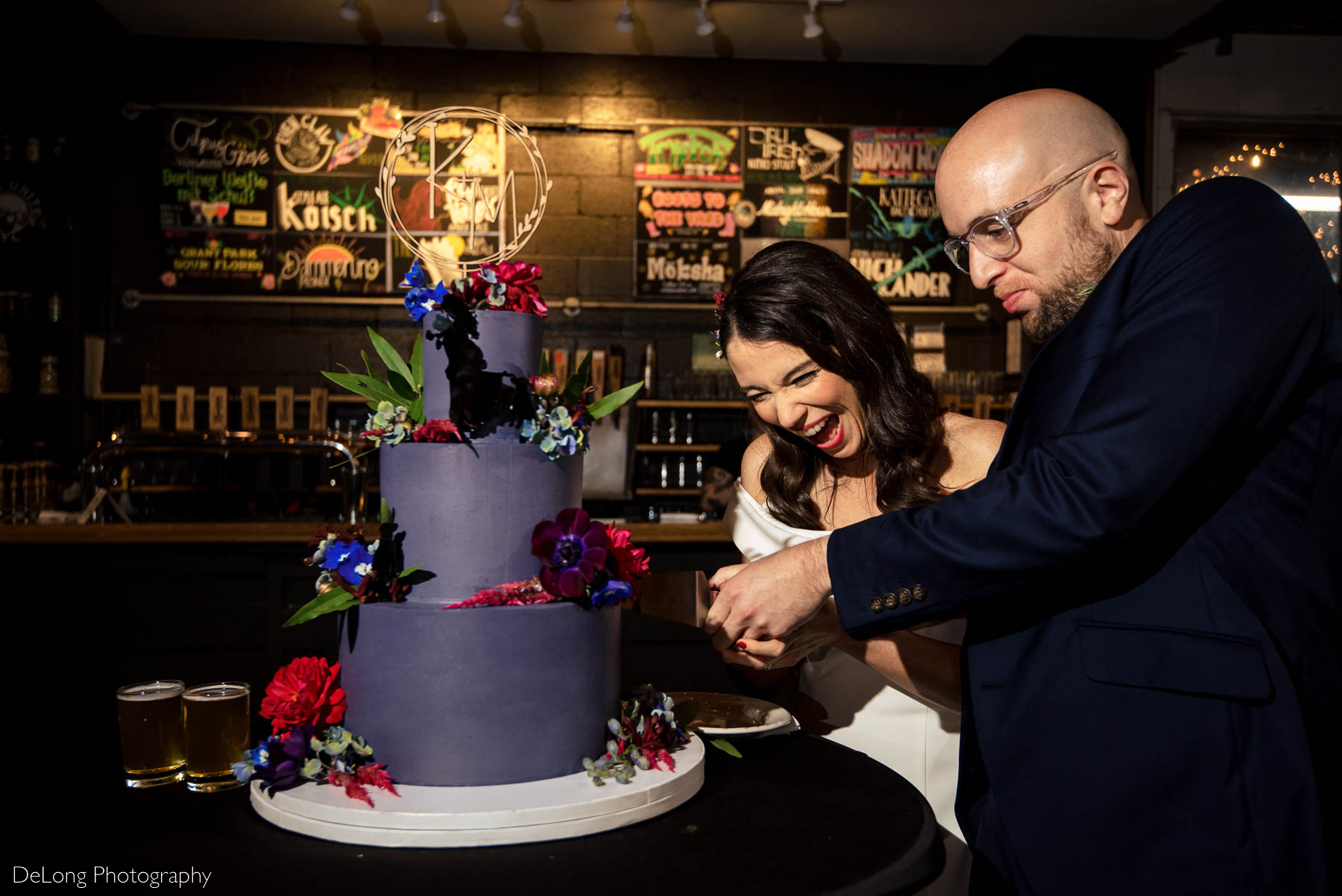 Bride and groom concentrating and laughing while cutting their jewel-toned purple wedding cake by Ginger Spice Bakery at Eventide Brewing in Atlanta, GA by Charlotte wedding Photographers DeLong Photography