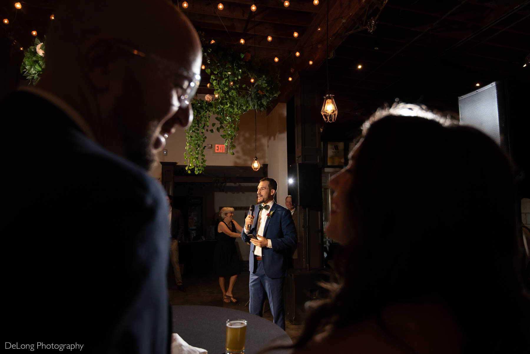 Bride and groom in foreground smiling at one another while a groomsmen gives his toast during their reception at Eventide Brewing in Atlanta, GA by Charlotte wedding Photographers DeLong Photography