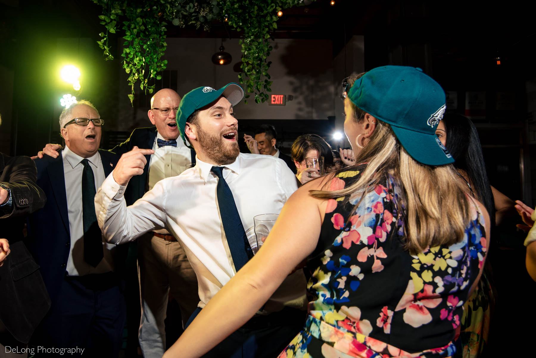Two guests smiling and dancing together on the dance floor wearing Atlanta Falcons hats at Eventide Brewing in Atlanta, GA by Charlotte wedding Photographers DeLong Photography