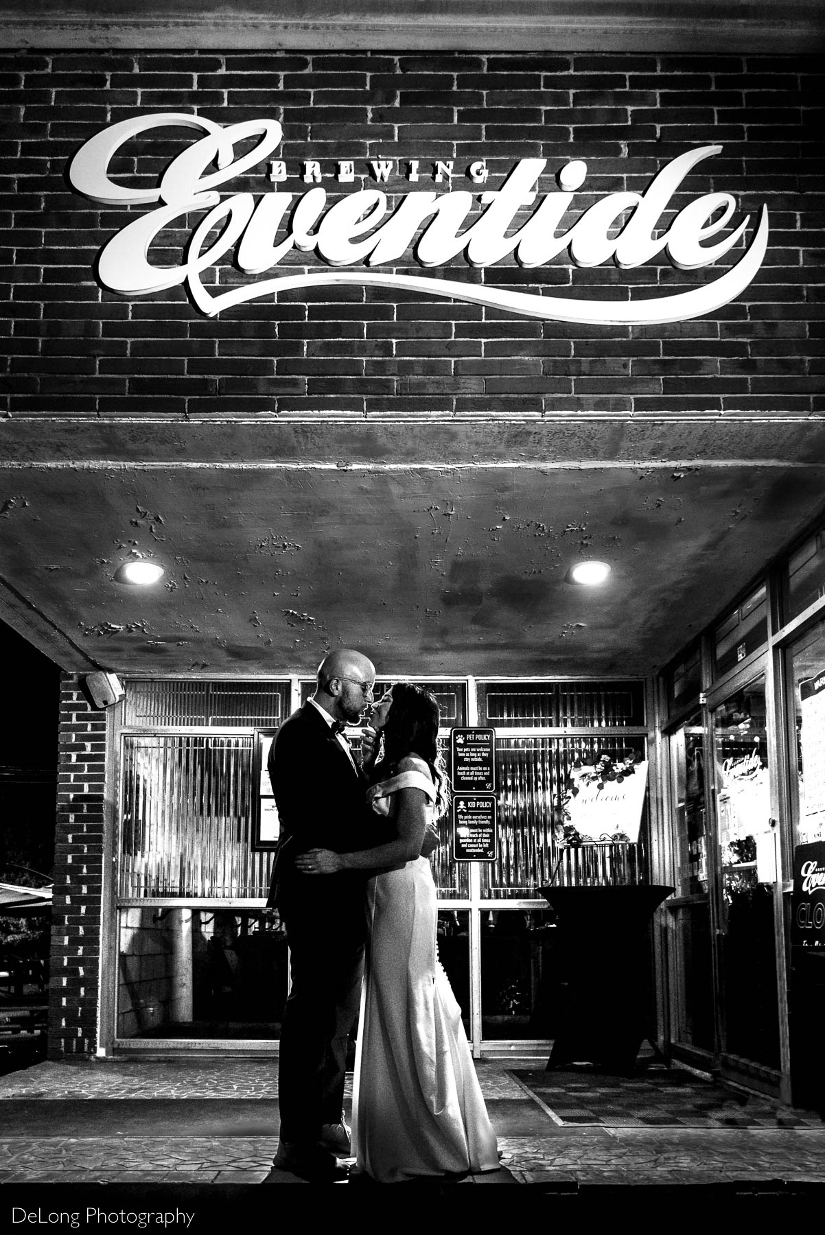 Black and white portrait of a bride and groom just about to kiss underneath the Eventide Brewing sign outside Eventide Brewing in Atlanta, GA by Charlotte wedding Photographers DeLong Photography