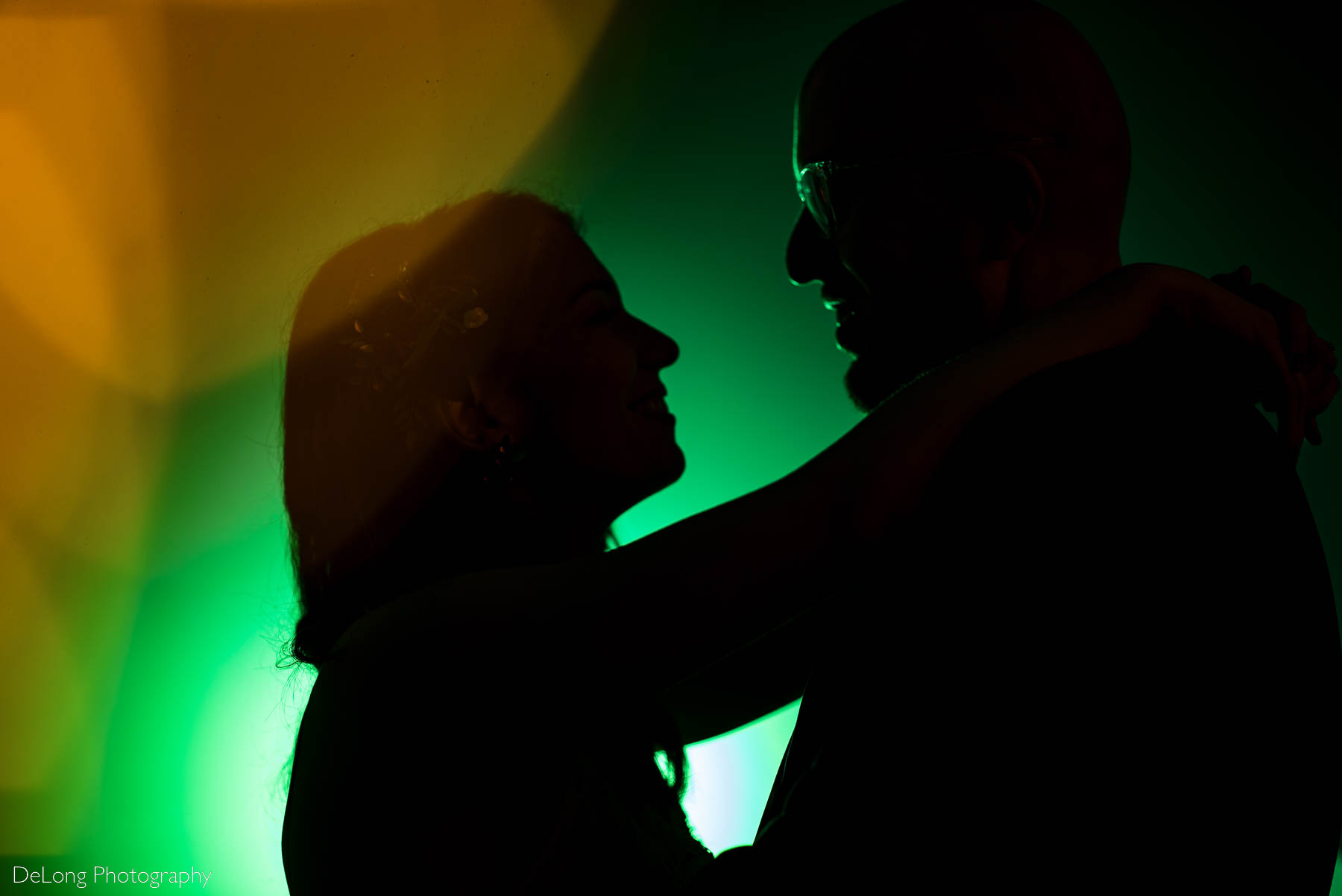 Silhouette of bride and groom smiling at one another in front of a green background with bokeh balls in the foreground at Eventide Brewing in Atlanta, GA by Charlotte wedding Photographers DeLong Photography