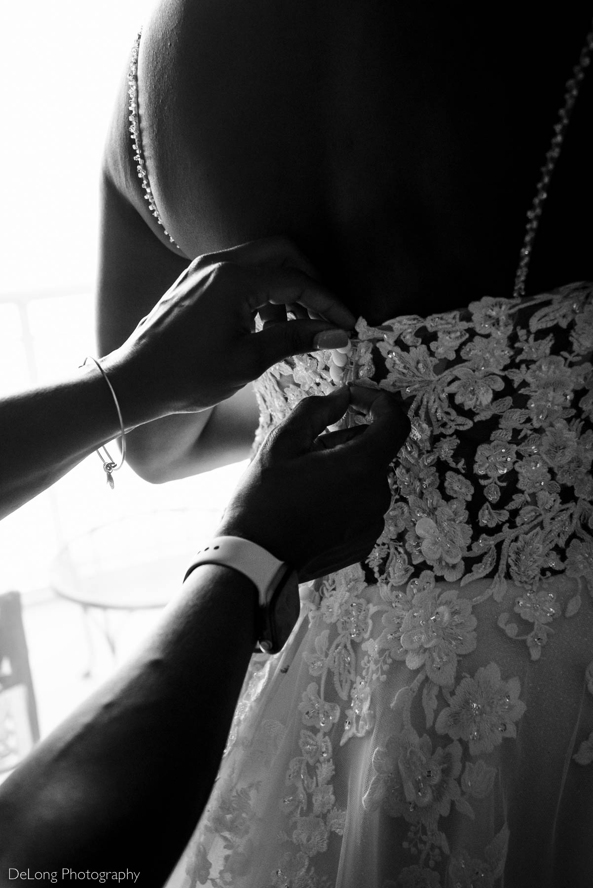 Black and white close-up photograph of the bride's friend's hands zipping up her wedding dress at the Ballantyne Hotel by Charlotte wedding photographers DeLong Photography