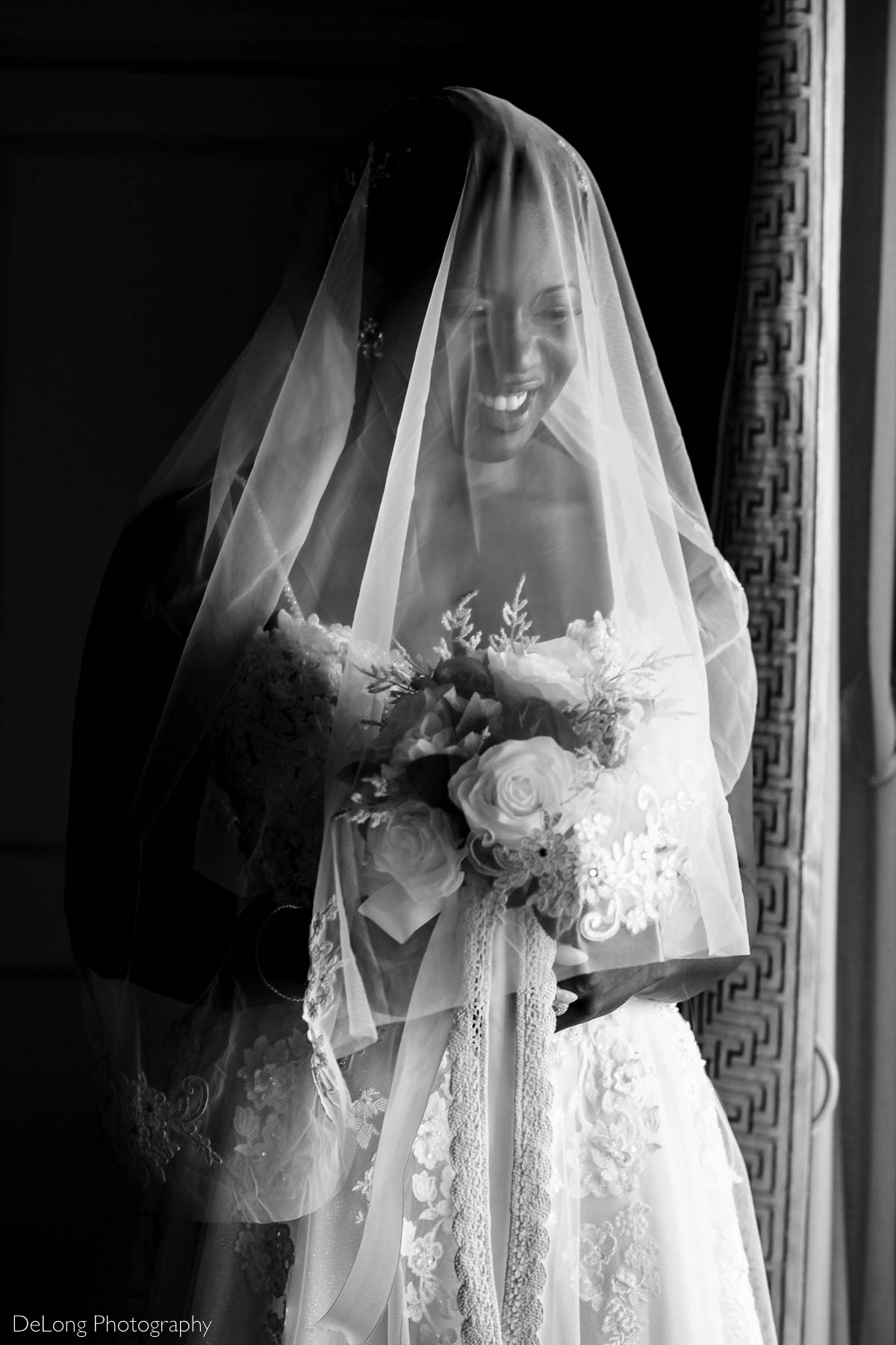 A black and white portrait of the bride under her veil smiling and holding her bouquet at the Ballantyne Hotel by Charlotte wedding photographers DeLong Photography