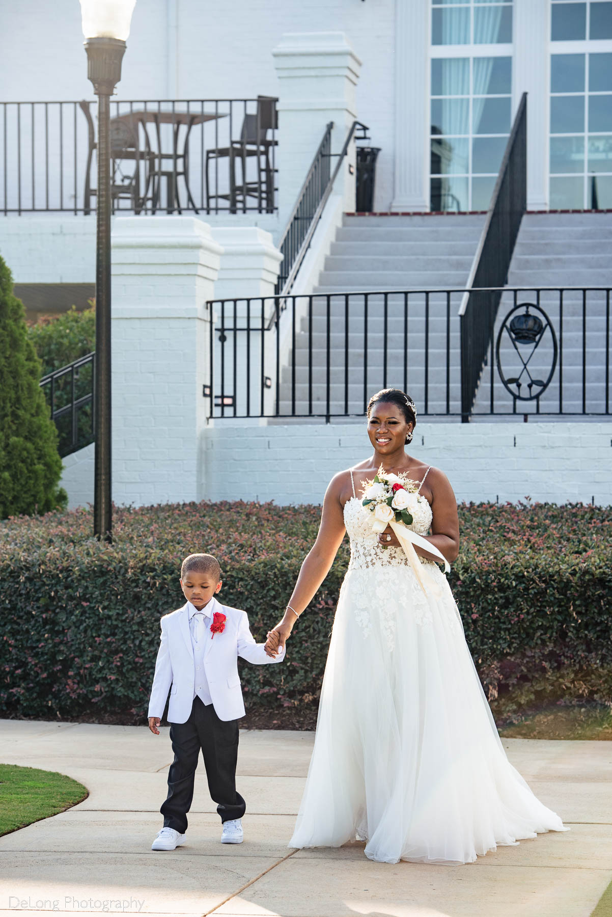 The bride walking down the aisle with one of her twin sons during the wedding ceremony at at Providence Country Club by Charlotte wedding photographers DeLong Photography