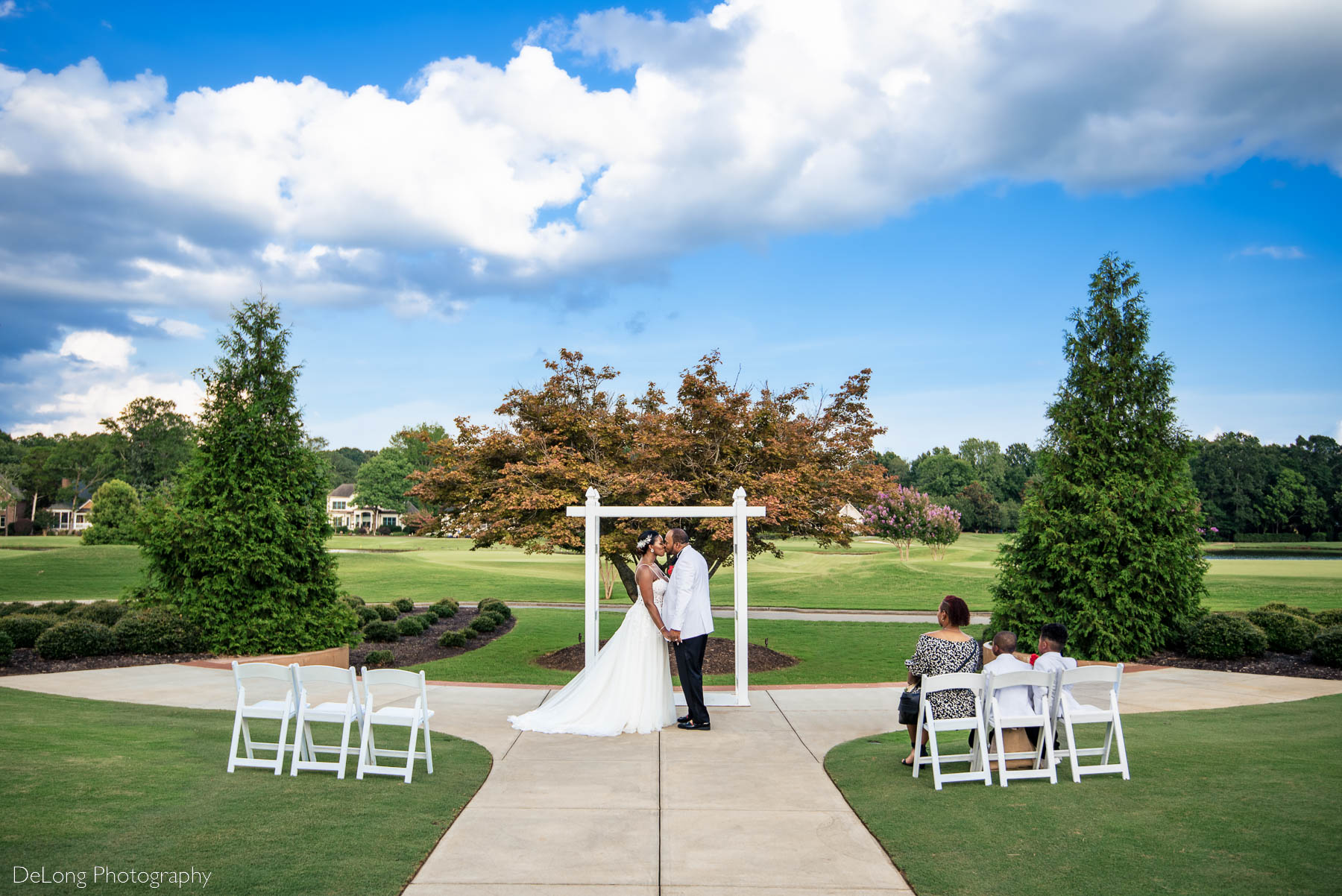 A wide angle photograph of the couple's first kiss at the conclusion of their elopement ceremony at Providence Country Club by Charlotte wedding photographers DeLong Photography