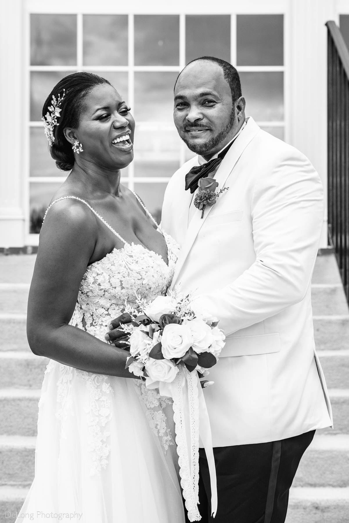 A black and white candid photograph of the bride and groom smiling and laughing on the steps at Providence Country Club by Charlotte wedding photographers DeLong Photography