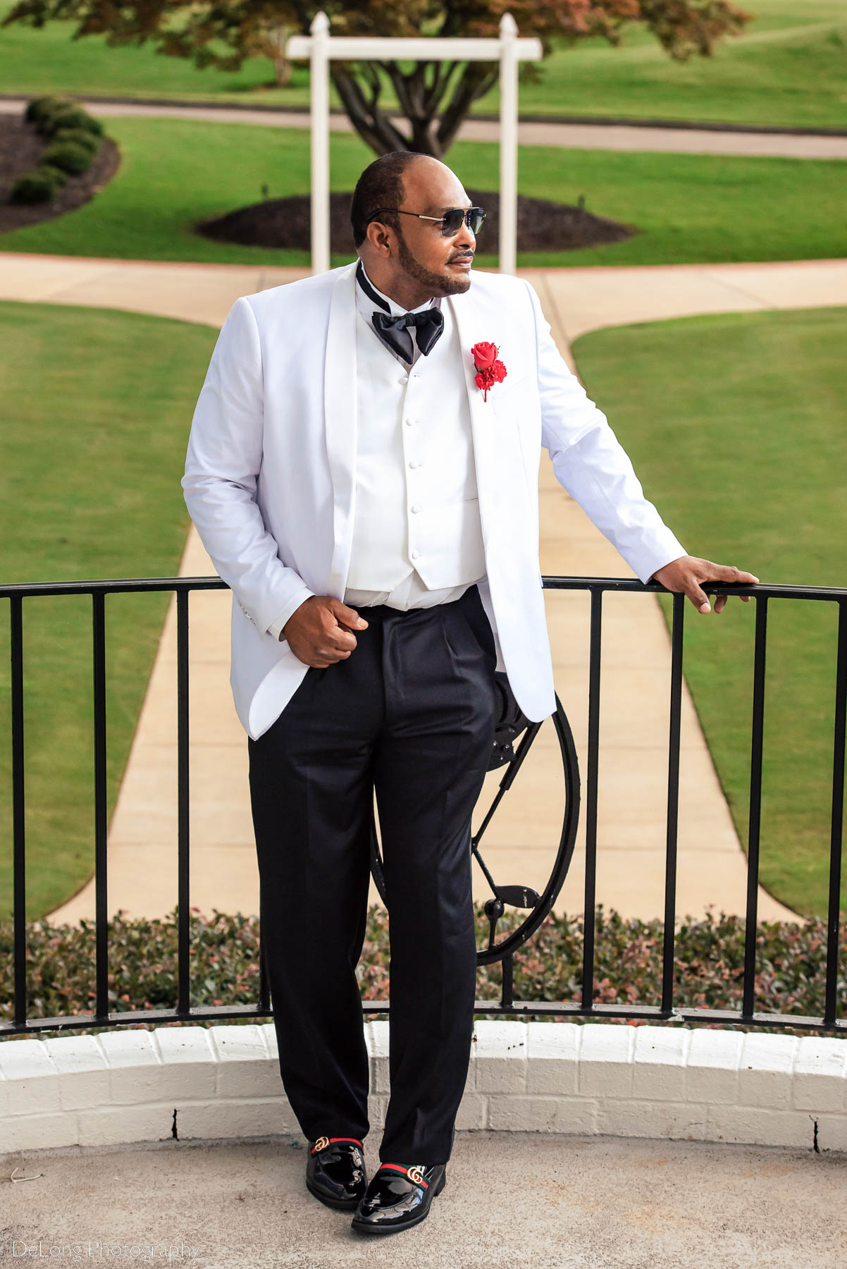 A stylized groom portrait where he's wearing sunglasses, a white jacket, and Gucci loafers at Providence Country Club by Charlotte wedding photographers DeLong Photography