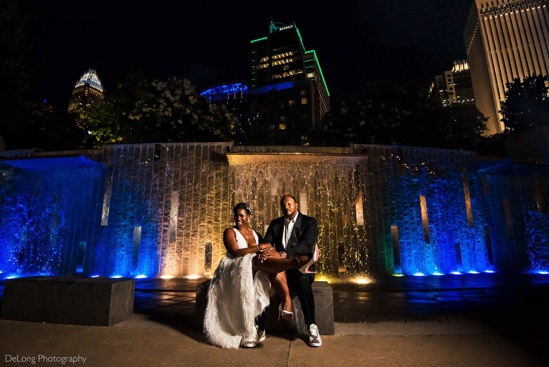 Black couple fun wedding portrait in front of a blue and yellow water feature at Romare Bearden Park in Uptown Charlotte, NC by Charlotte wedding photographers DeLong Photography