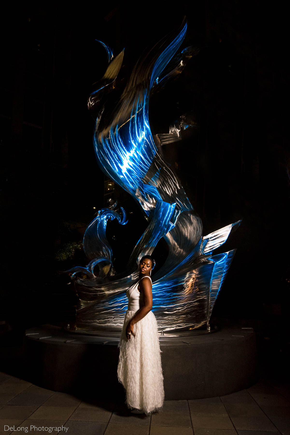 A bridal portrait  in front of a blue-lit sculpture at Romare Bearden Park in Uptown Charlotte, NC by Charlotte wedding photographers DeLong Photography