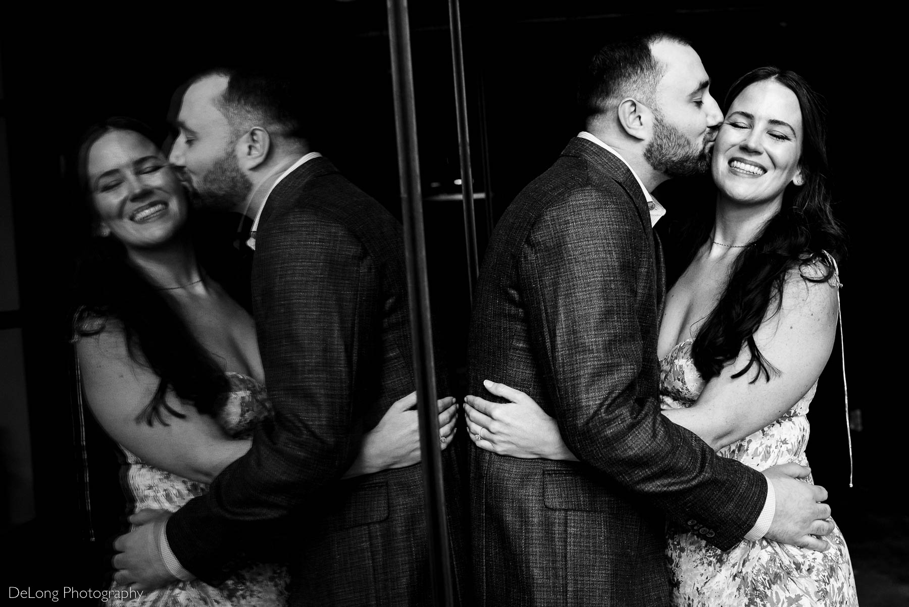 Black and white window reflection image of a man kissing his fiancée's cheek as she smiles with her eyes closed giggling at Westside Provisions in Atlanta by Charlotte Wedding Photographers DeLong Photography
