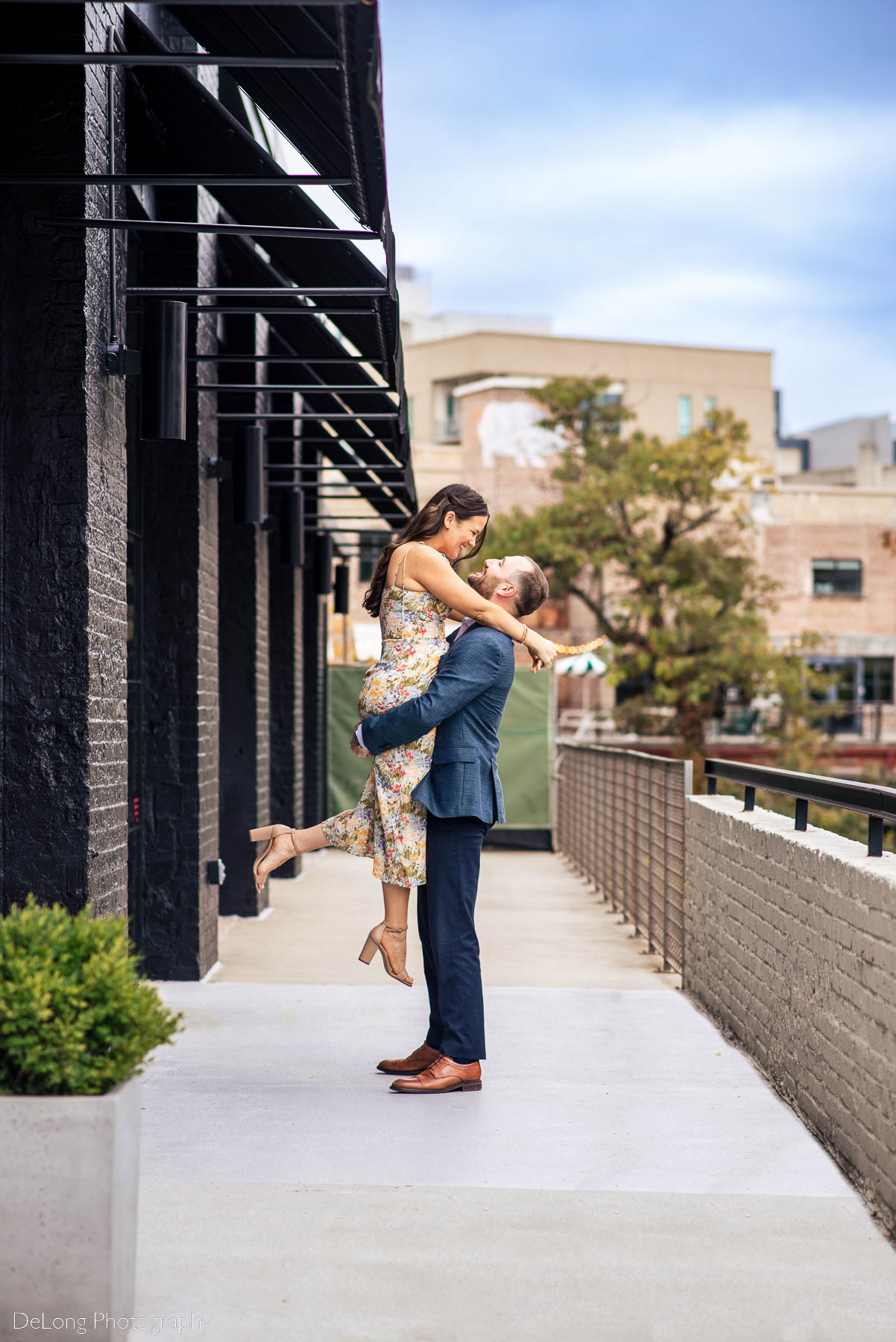Color photograph of a man lifting his fiancée up under the butt as they smile at one another at Westside Provisions in Atlanta by Charlotte Wedding Photographers DeLong Photography