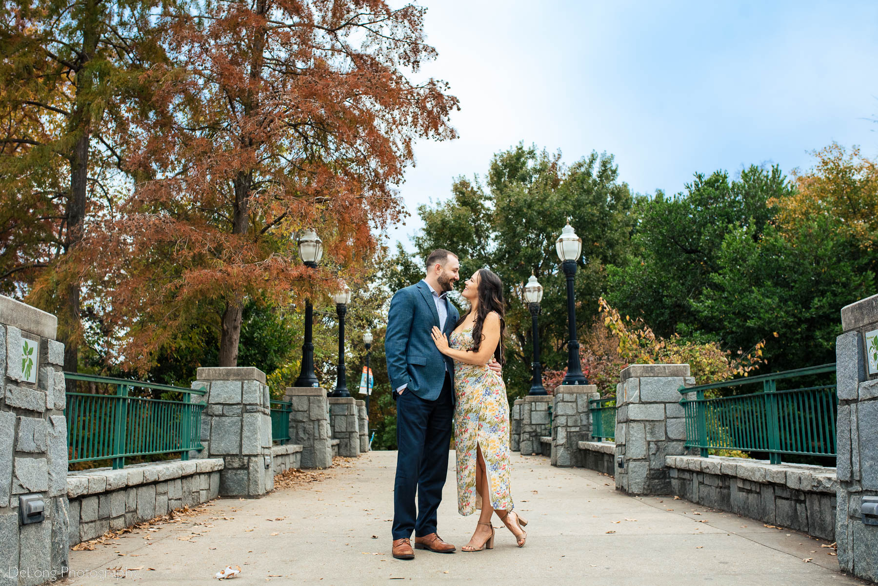Portrait of engaged couple softly smiling and looking at one another on a bridge adorned with lanterns at Piedmont Park in Atlanta by Charlotte wedding photographers DeLong Photography