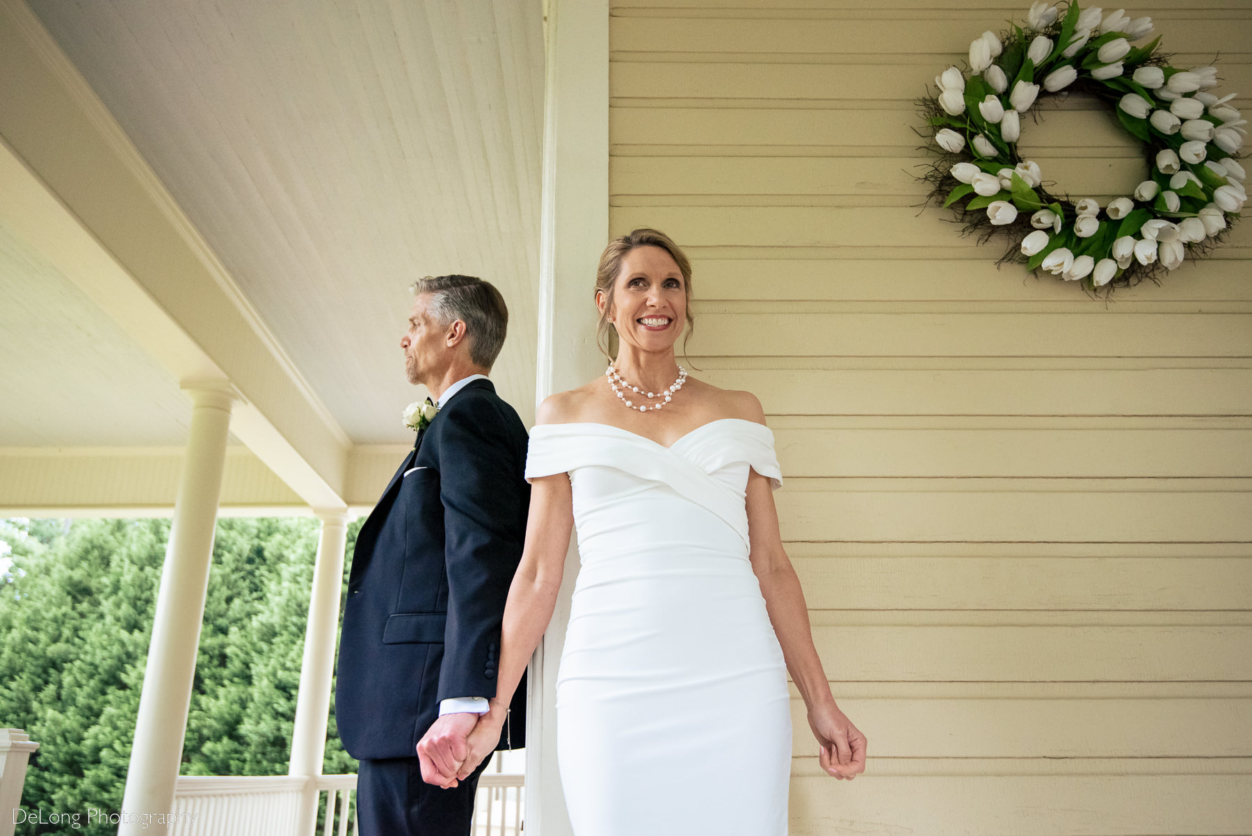 First touch on the porch of the main house at Alexander Homestead. Bride is smiling and excited. Photograph by Charlotte wedding photographers DeLong Photography.