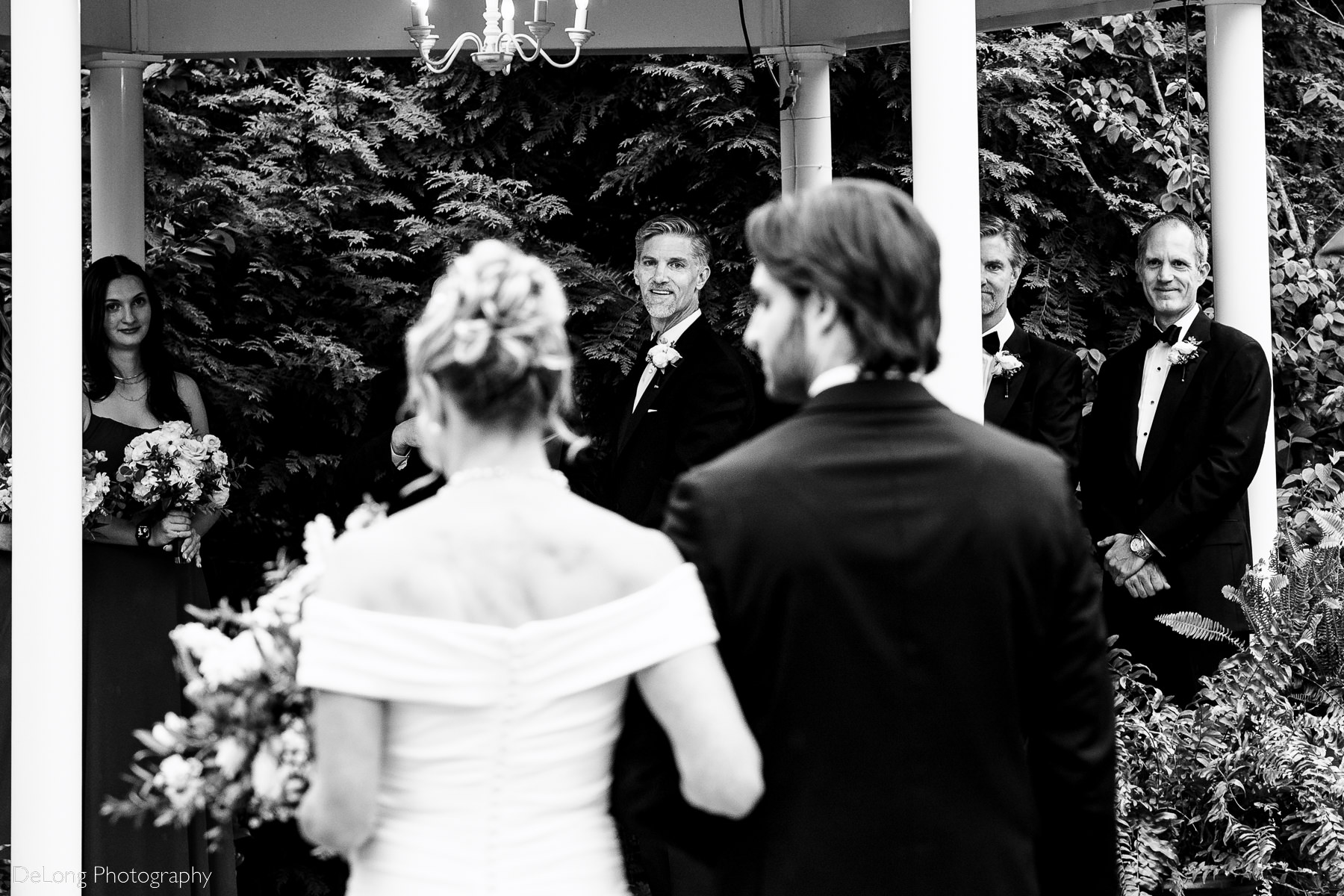 Black and white candid photograph of groom turning around to see his bride coming down the aisle. The groom's face is framed between the bride and her son as they make their way down the aisle. Photograph by Charlotte wedding photographers DeLong Photography.