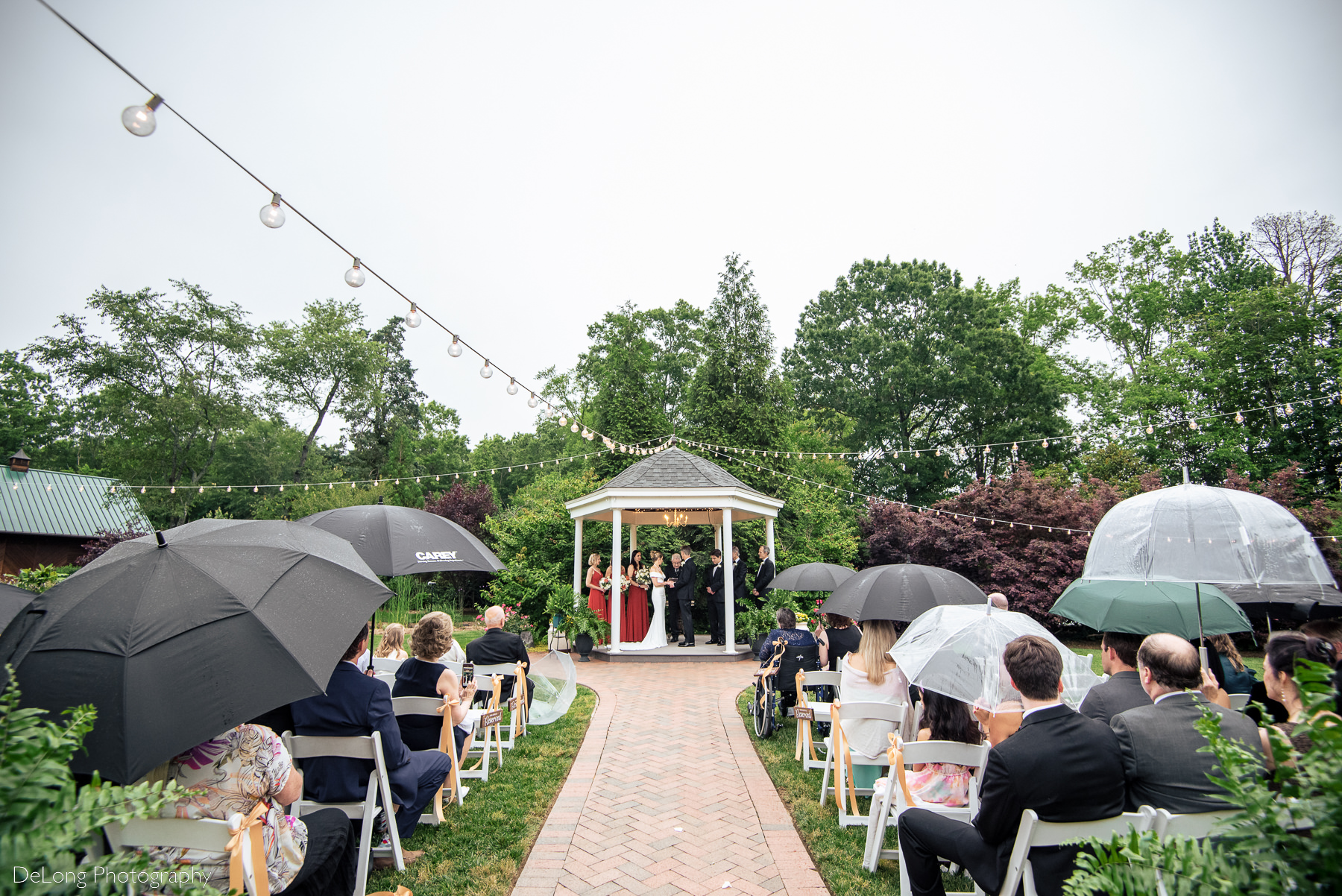 Wide outdoor ceremony photograph taken during a wedding at Alexander Homestead on a rainy day. Photograph by Charlotte wedding photographers DeLong Photography.