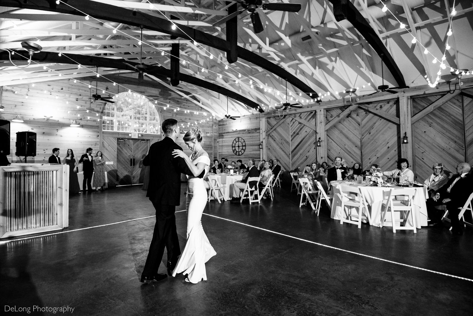 Black and white candid photograph of bride smiling while working through the choreographed first dance with her groom. Photograph taken at Alexander Homestead by Charlotte wedding photographers DeLong Photography.