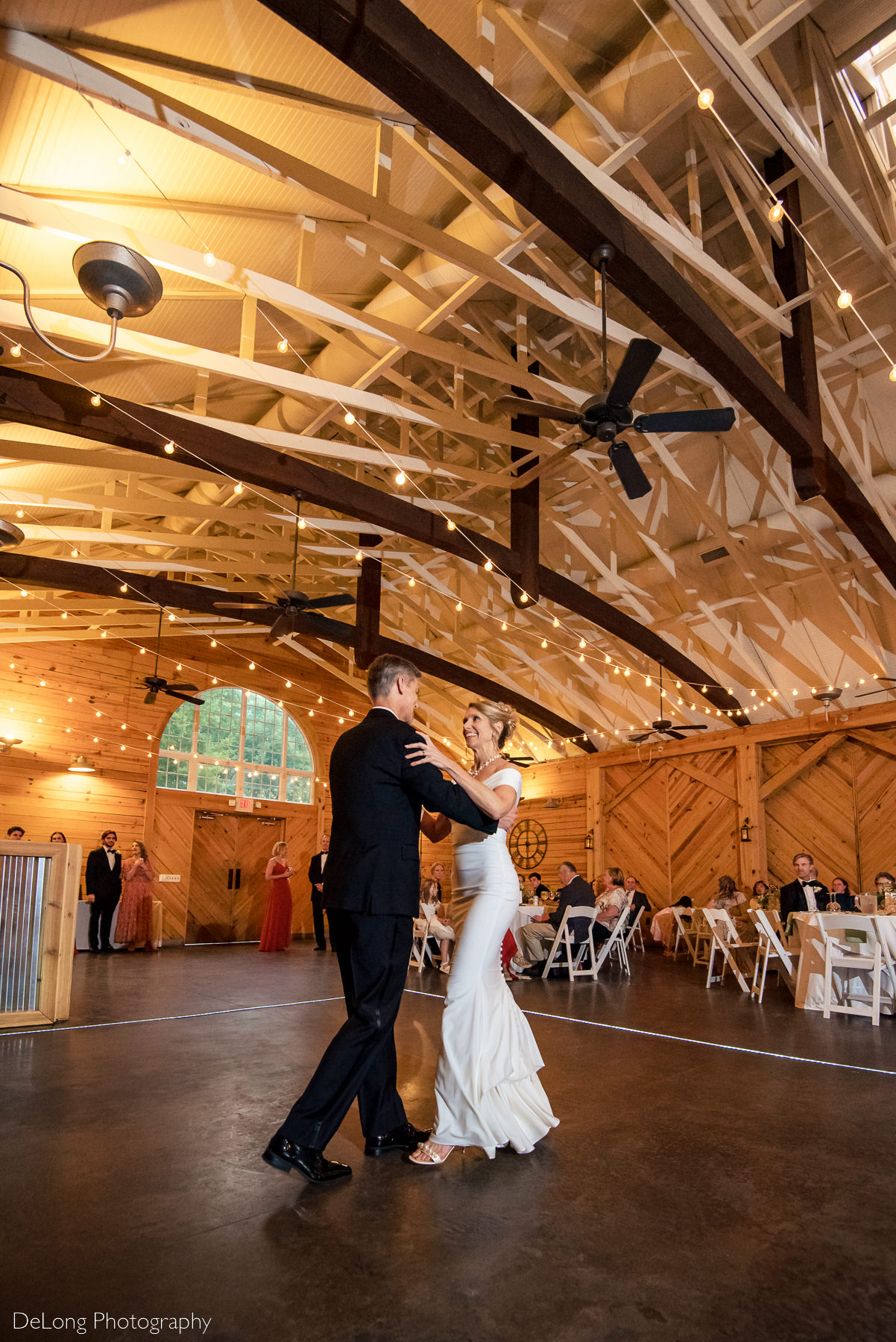 Wide-angle photograph of bride and groom smiling at one another during their first dance at Alexander Homestead. Photograph by Charlotte wedding photographers DeLong Photography.