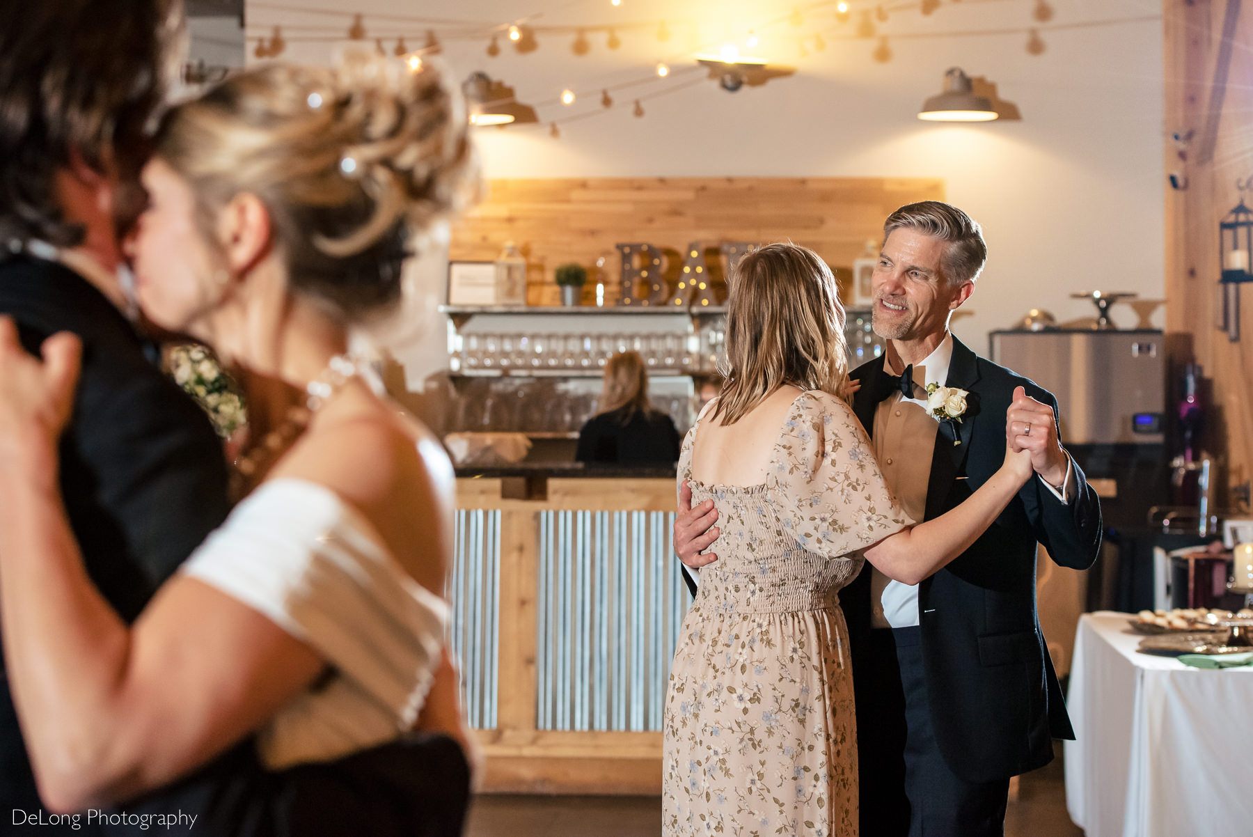 Father smiling during the parent dance during a wedding reception at Alexander Homestead. The bride dancing with her son is in the foreground. Photograph by Charlotte wedding photographers DeLong Photography.