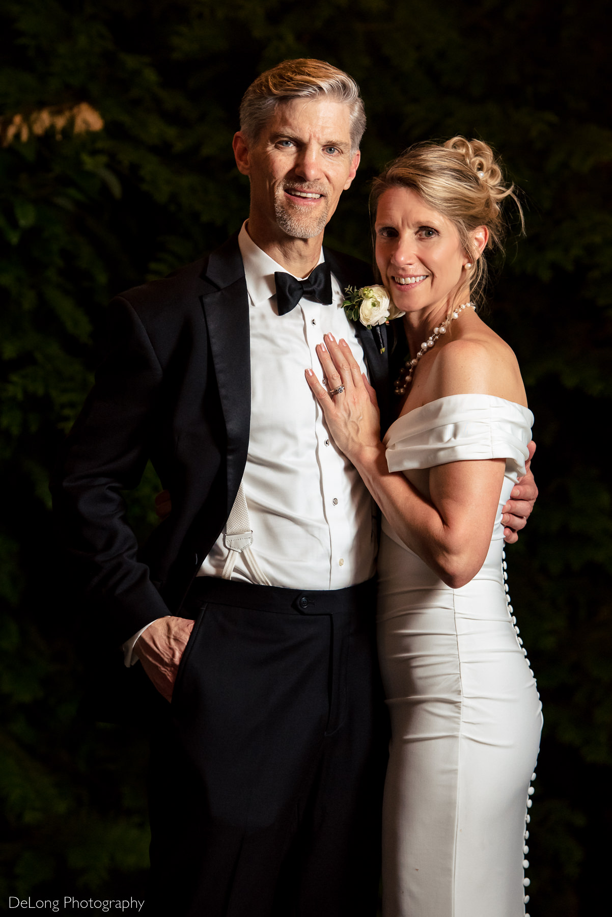 Traditional portrait taken at night in the gazebo of Alexander Homestead. The bride and groom have their arms around each other and are smiling directly at the camera. Photograph by Charlotte wedding photographers DeLong Photography.