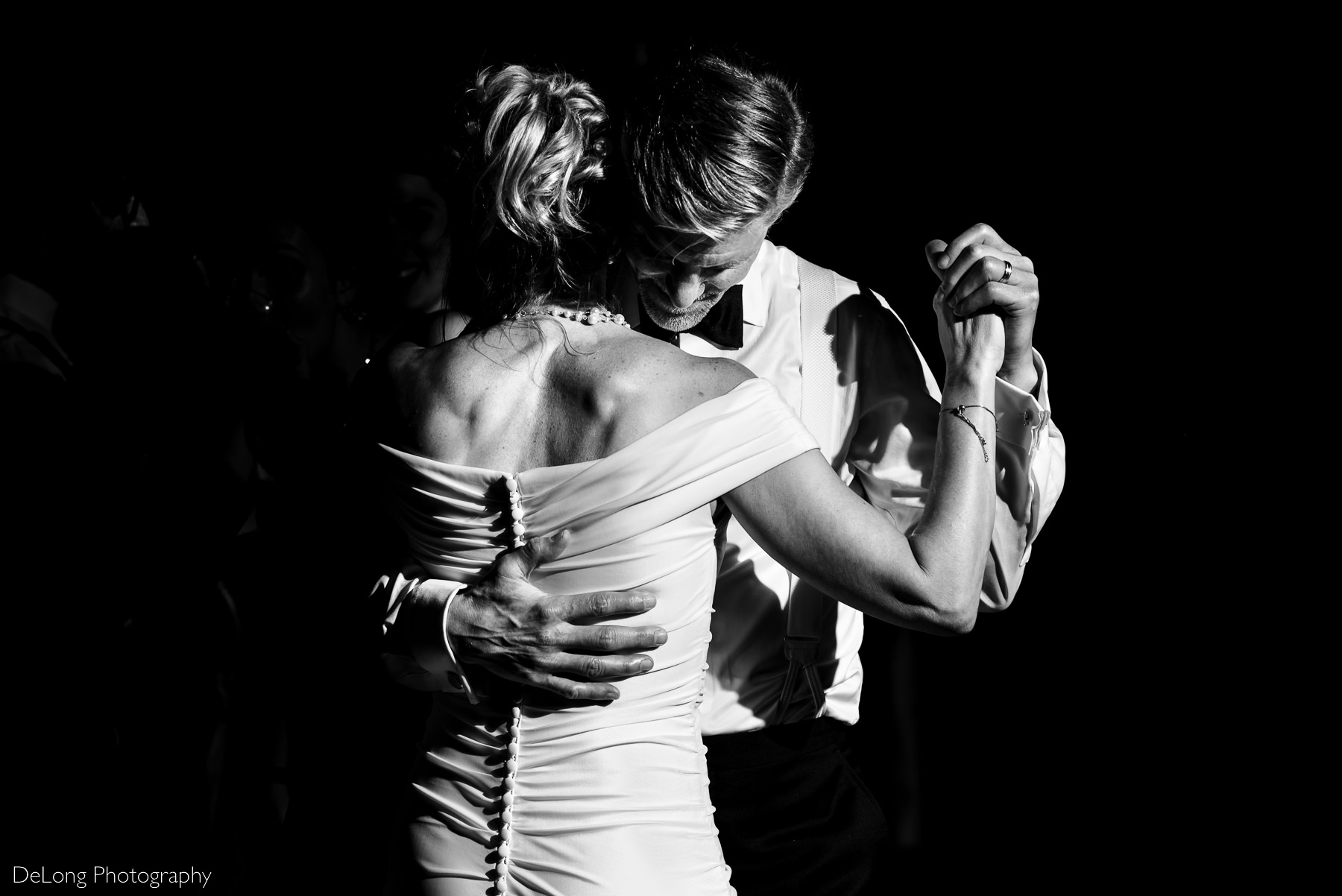 Black and white candid photograph of a groom holding his bride close during their private dance at the end of their wedding reception. Black and white nighttime silhouette of a couple with their foreheads together, standing inside the gazebo at Alexander Homestead. Photo by Charlotte wedding photographers DeLong Photography.