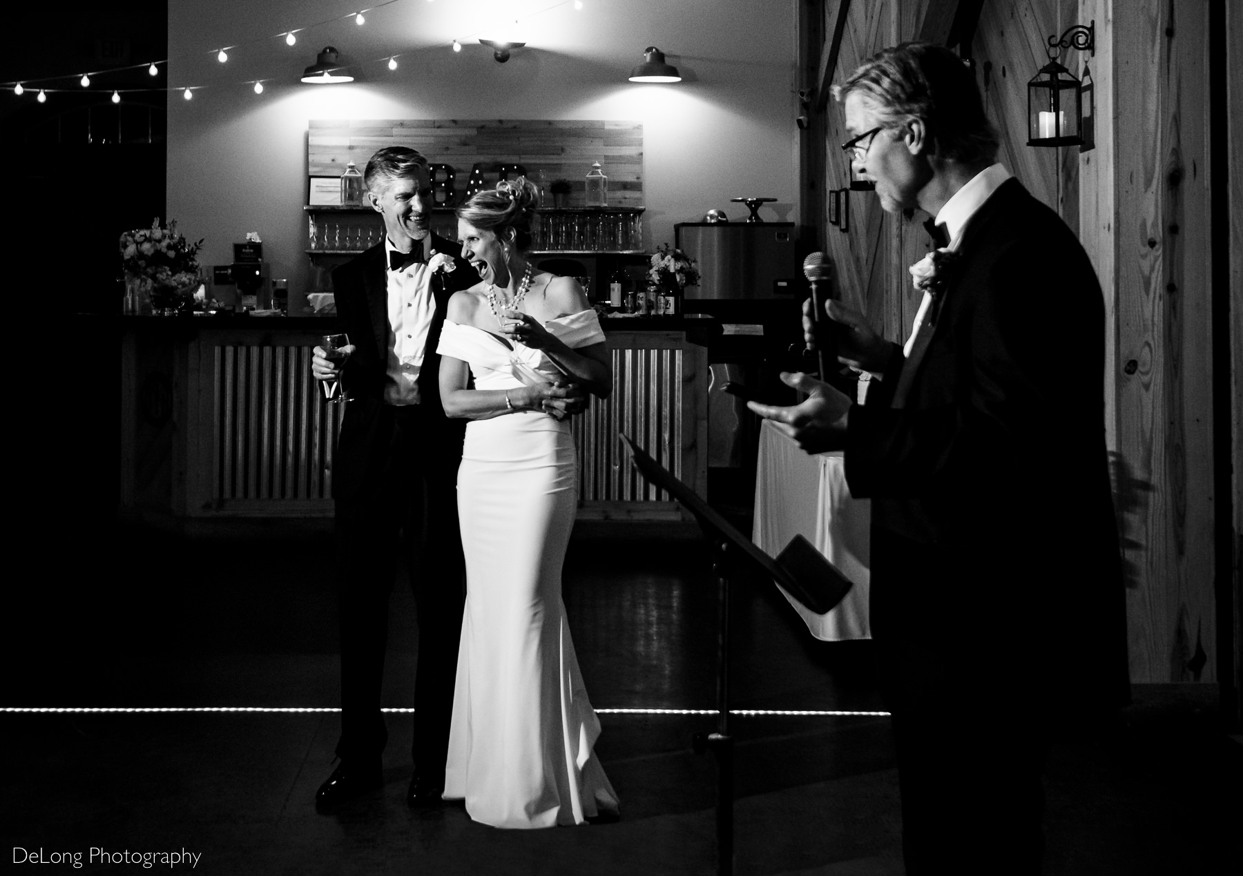 Black and white candid photograph of a bride cracking up laughing during the Best Man speech at a wedding reception at Alexander Homestead. Photograph by Charlotte wedding photographers DeLong Photography.