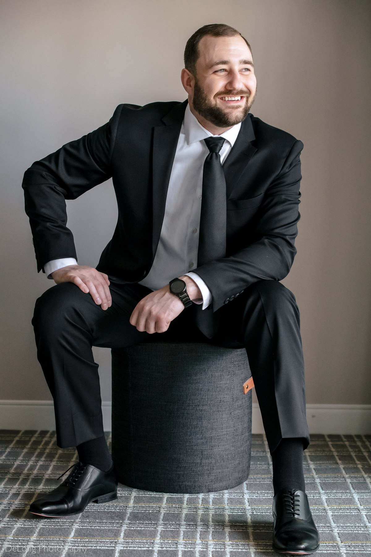 Portrait of groom seated and smiling looking out the window by Charlotte wedding photographers DeLong Photography