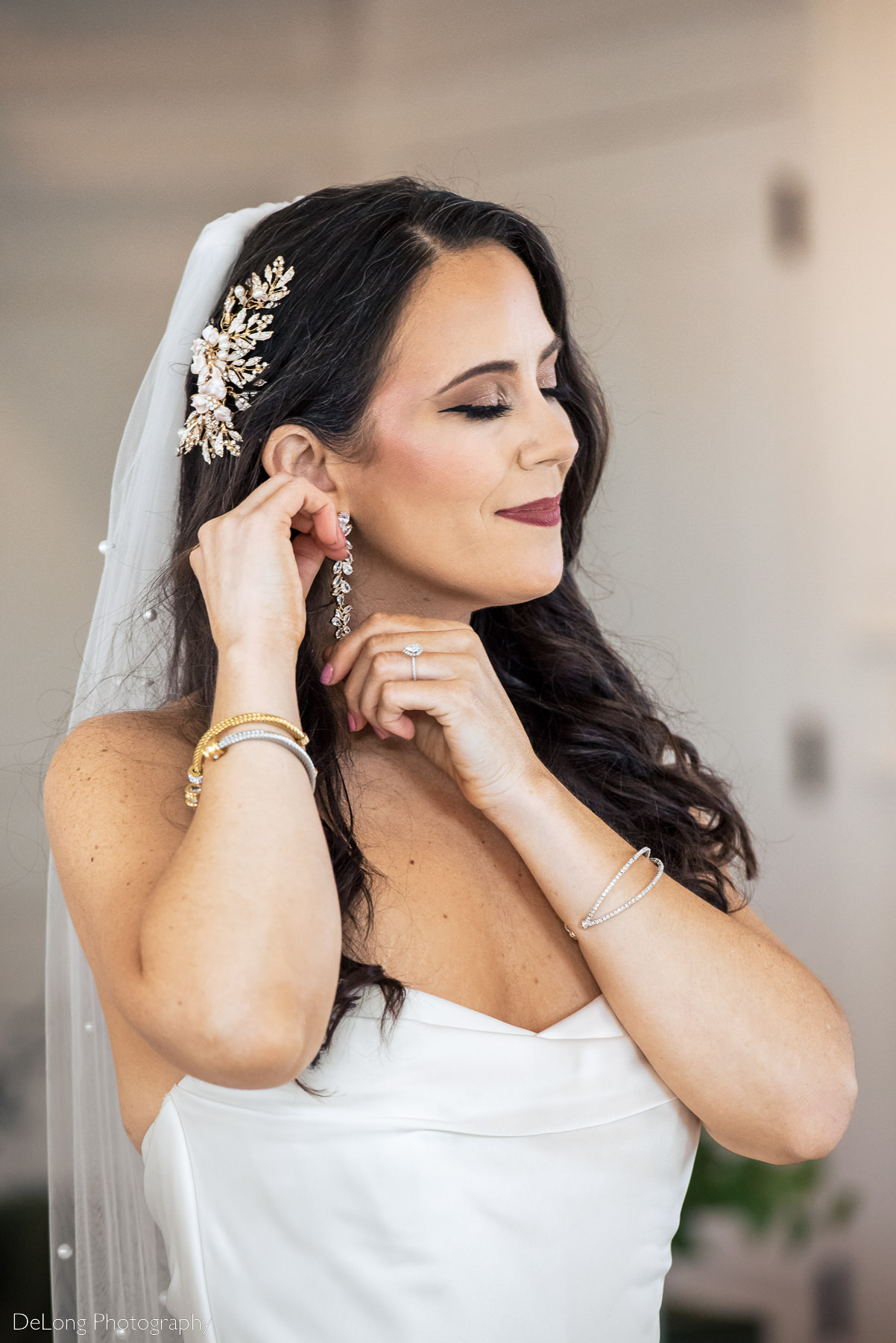 Portrait of a bride smiling and touching her long jeweled earrings, and showcasing her jeweled hairpin, at Upstairs Atlanta by Charlotte wedding photographers DeLong Photography