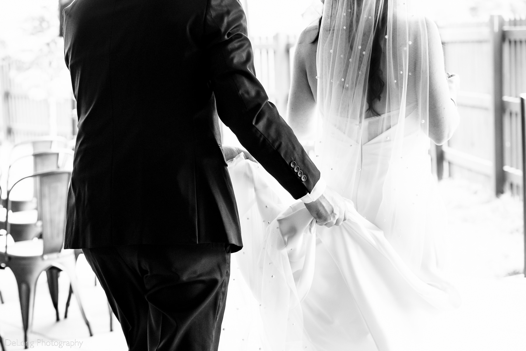 Black and white candid photograph of groom helping the bride with her train while walking around for portraits at Upstairs Atlanta by Charlotte wedding photographers DeLong Photography