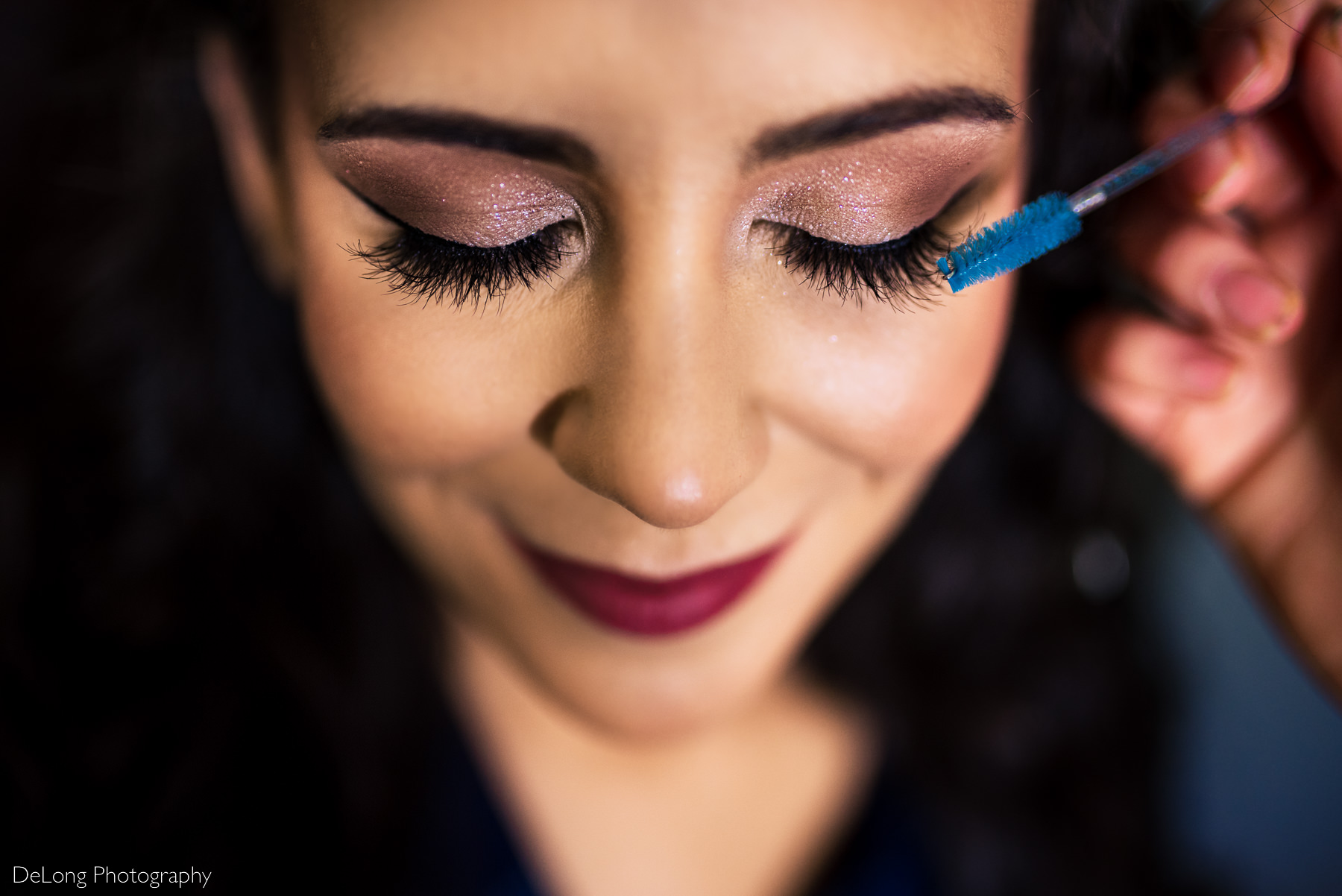 top down photo focused on smiling bride's eyelashes as mascara is applied showing off her sparkly pint eyeshadow by Charlotte wedding photographers DeLong Photography