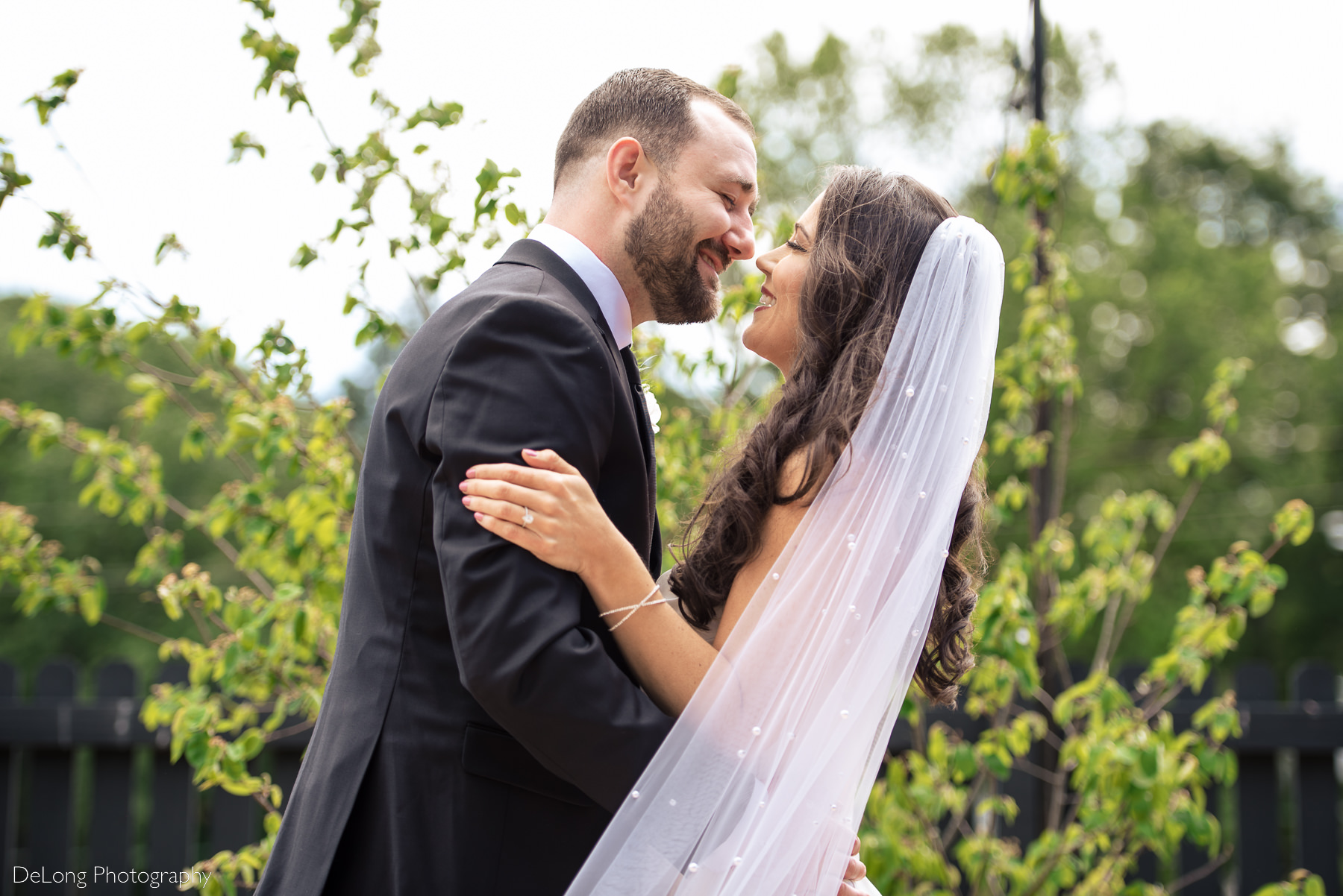 Bridge and groom facing one another smiling at one another in front of greenery at Upstairs Atlanta by Charlotte wedding photographers DeLong Photography