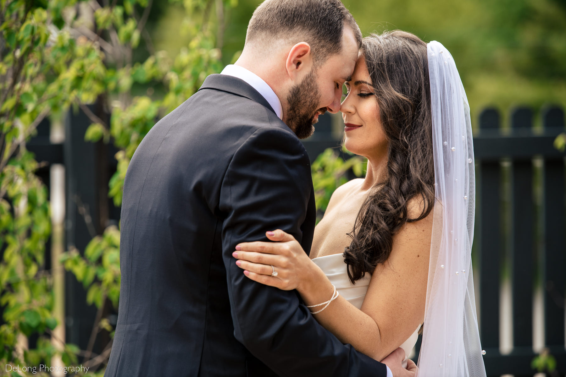 Bride and groom with their foreheads together and soft smiles among greenery outside Upstairs Atlanta by Charlotte wedding photographers DeLong Photography