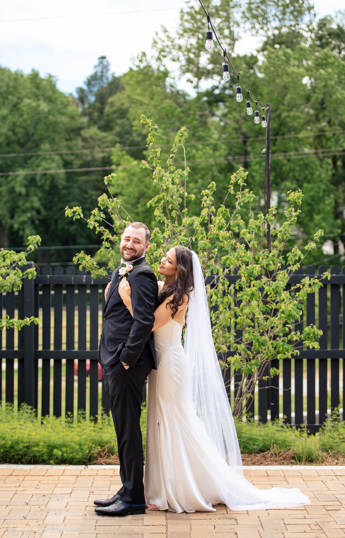 Bridge hugging groom from behind as he smiles looking back toward her outside on the patio of Upstairs Atlanta by Charlotte wedding photographers DeLong Photography