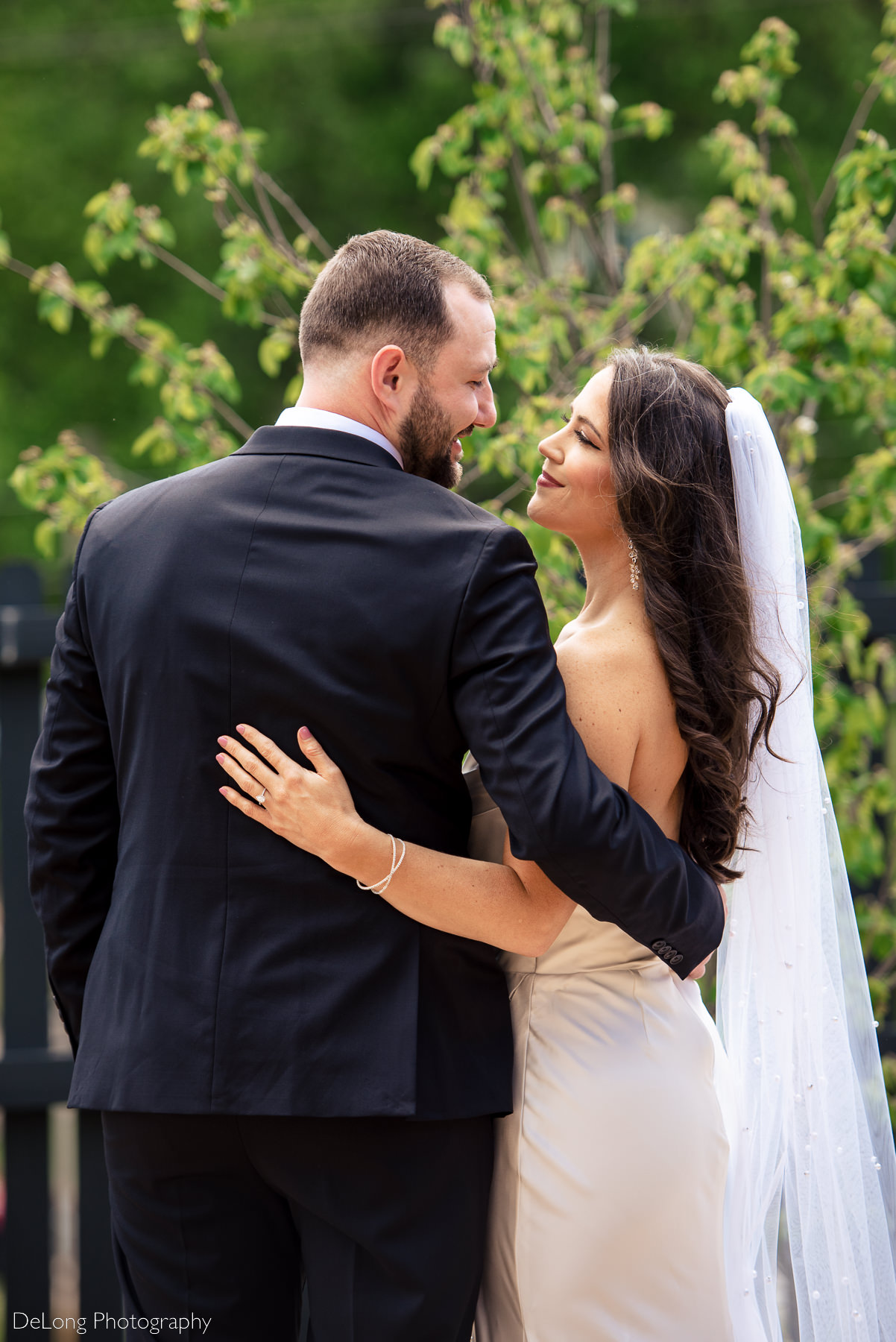 Bride and groom with their backs toward the camera, arms around each other. They are smiling and looking into each others eyes in front of greenery outside Upstairs Atlanta. Photograph by Charlotte wedding photographers DeLong Photography 