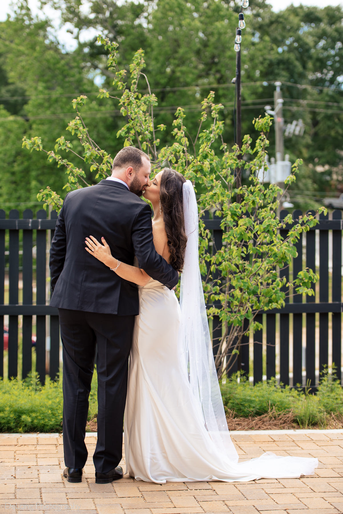 Bride and groom with their arms around each other, facing away from the camera. They are sharing a kiss. Photograph by Charlotte wedding photographers DeLong Photography