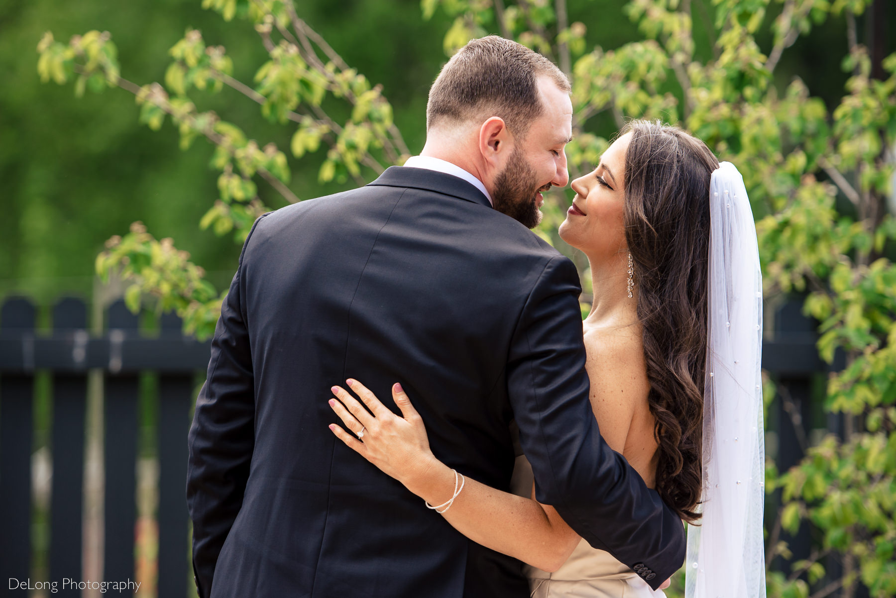 Bride and groom with their arms around each other, facing away from the camera. They are giving each other eskimo kisses and smiling. Photograph by Charlotte wedding photographers DeLong Photography.