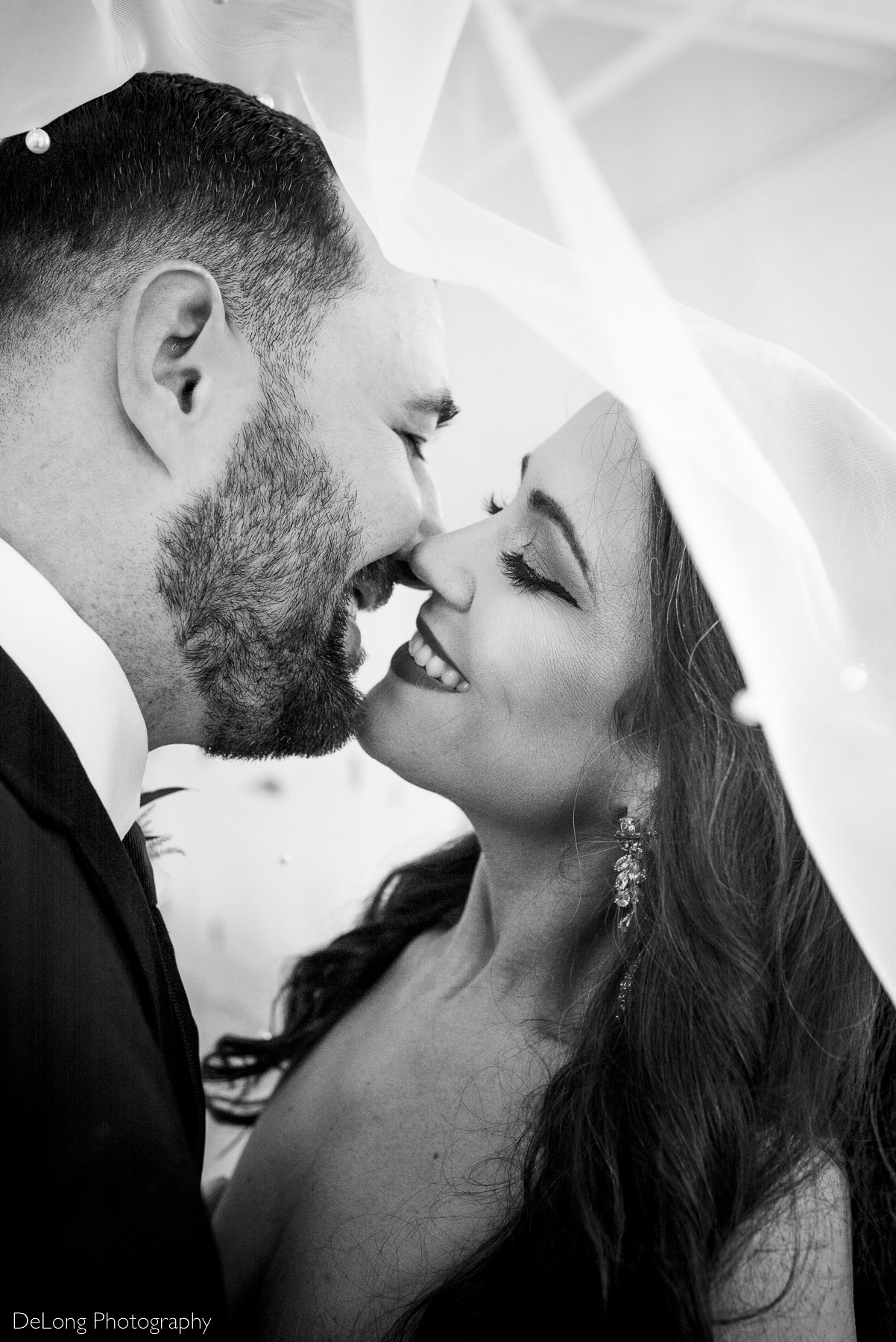 Up close vertical photograph of a bride and groom smiling just before a kiss, under her veil. Photograph by Charlotte wedding photographers DeLong Photography.