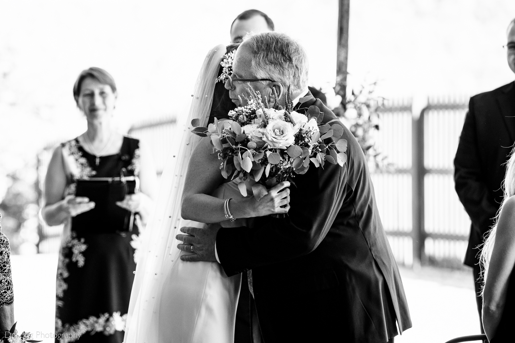 Black and white photograph of a bride and her father hugging as he gives her away during the ceremony at Upstairs Atlanta. Photograph by Charlotte wedding photographers DeLong Photography.